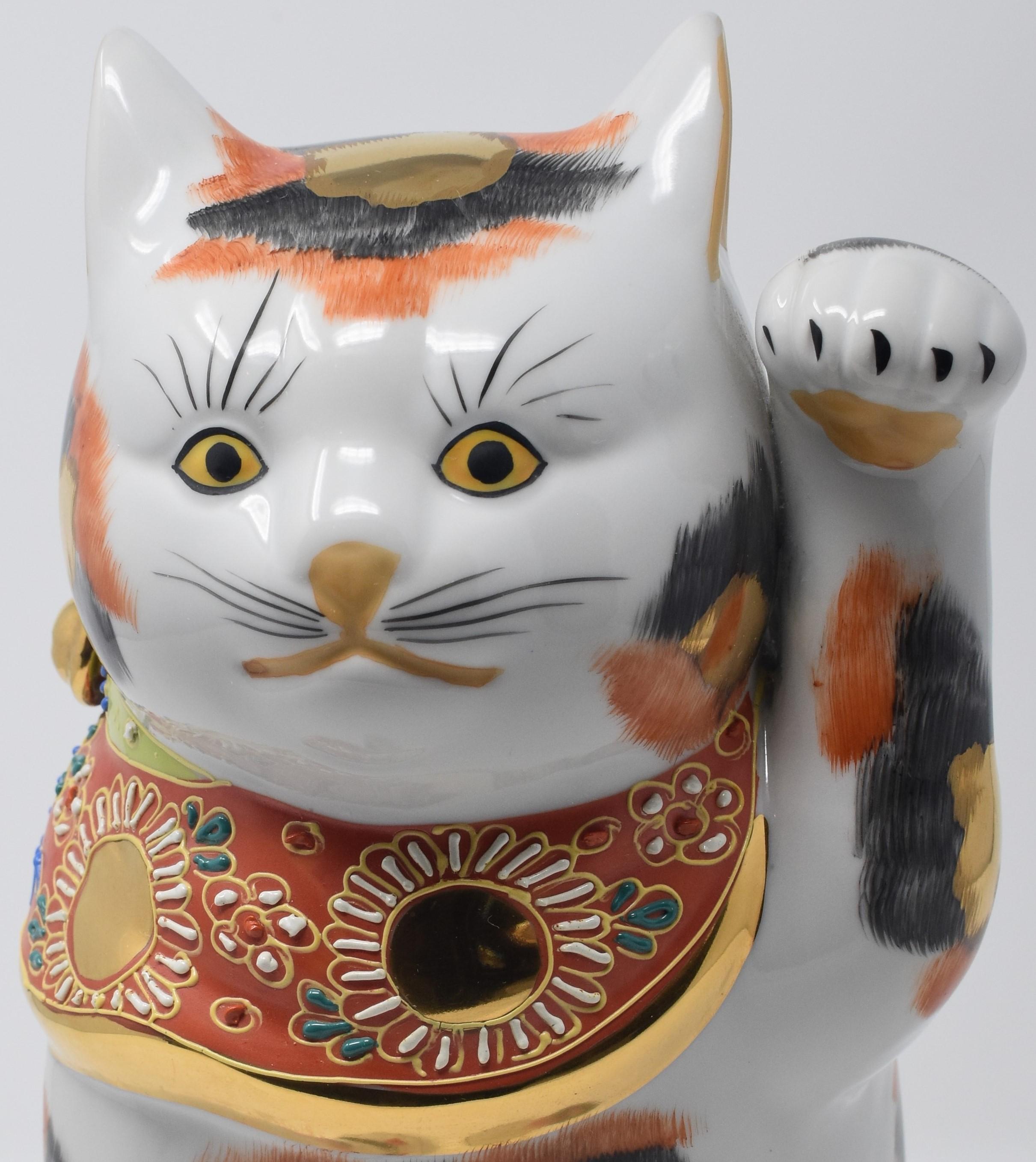 Charming beckoning cat with left paw raised is a gilded and hand painted porcelain piece from the Kutani region of Japan.
The beckoning cat comes in two varieties. The more common right-handed beckoning cat (with right paw raised) is said to bring