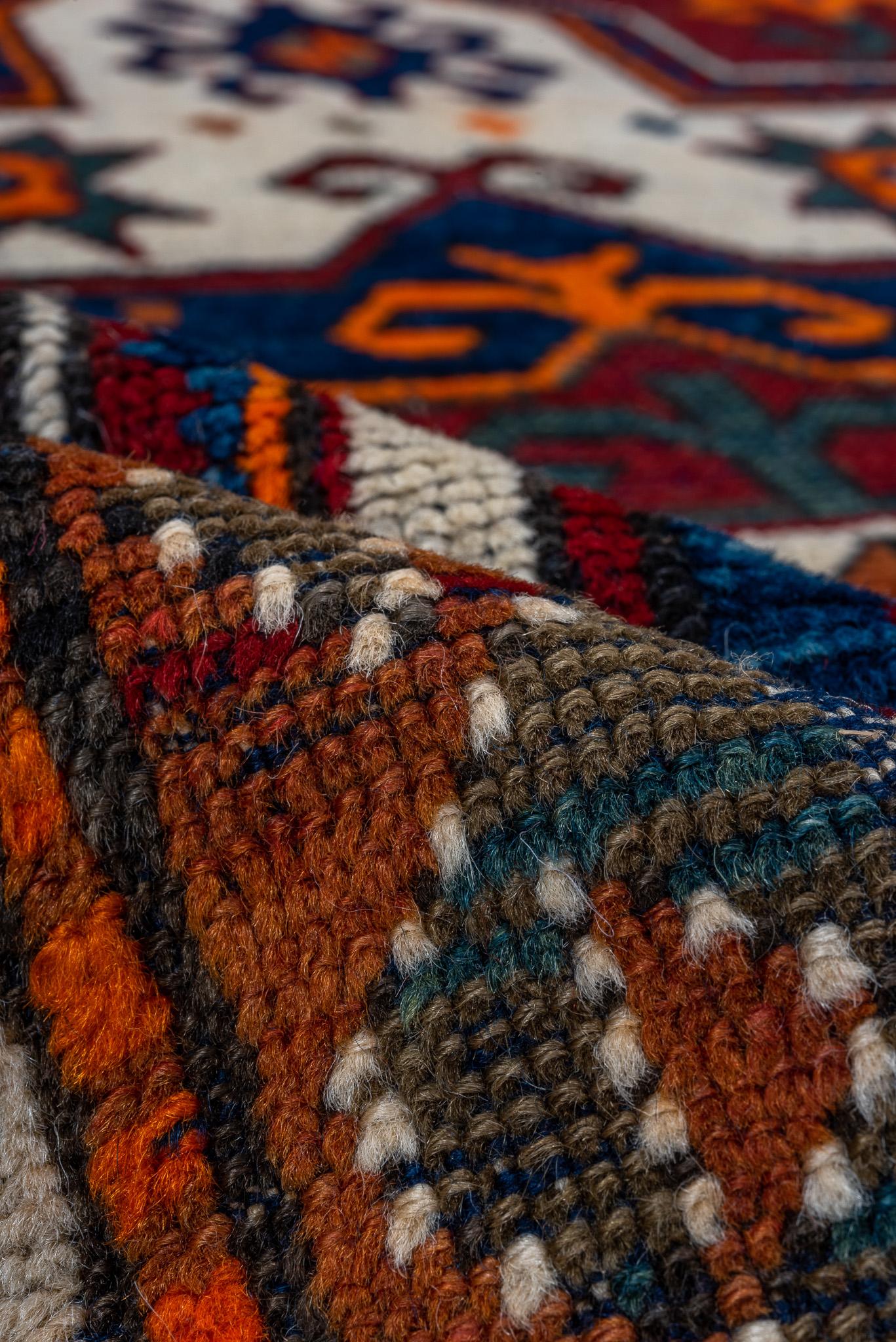 Dies ist ein lebendiger Kazak-Teppich mit den Maßen 3,1 x 4,9 Fuß. Es zeigt ein kühnes zentrales Medaillon mit geometrischen Motiven in auffälligen Farben wie Rot, Blau, Orange und Elfenbein. Die detaillierte Umrandung ergänzt das komplizierte