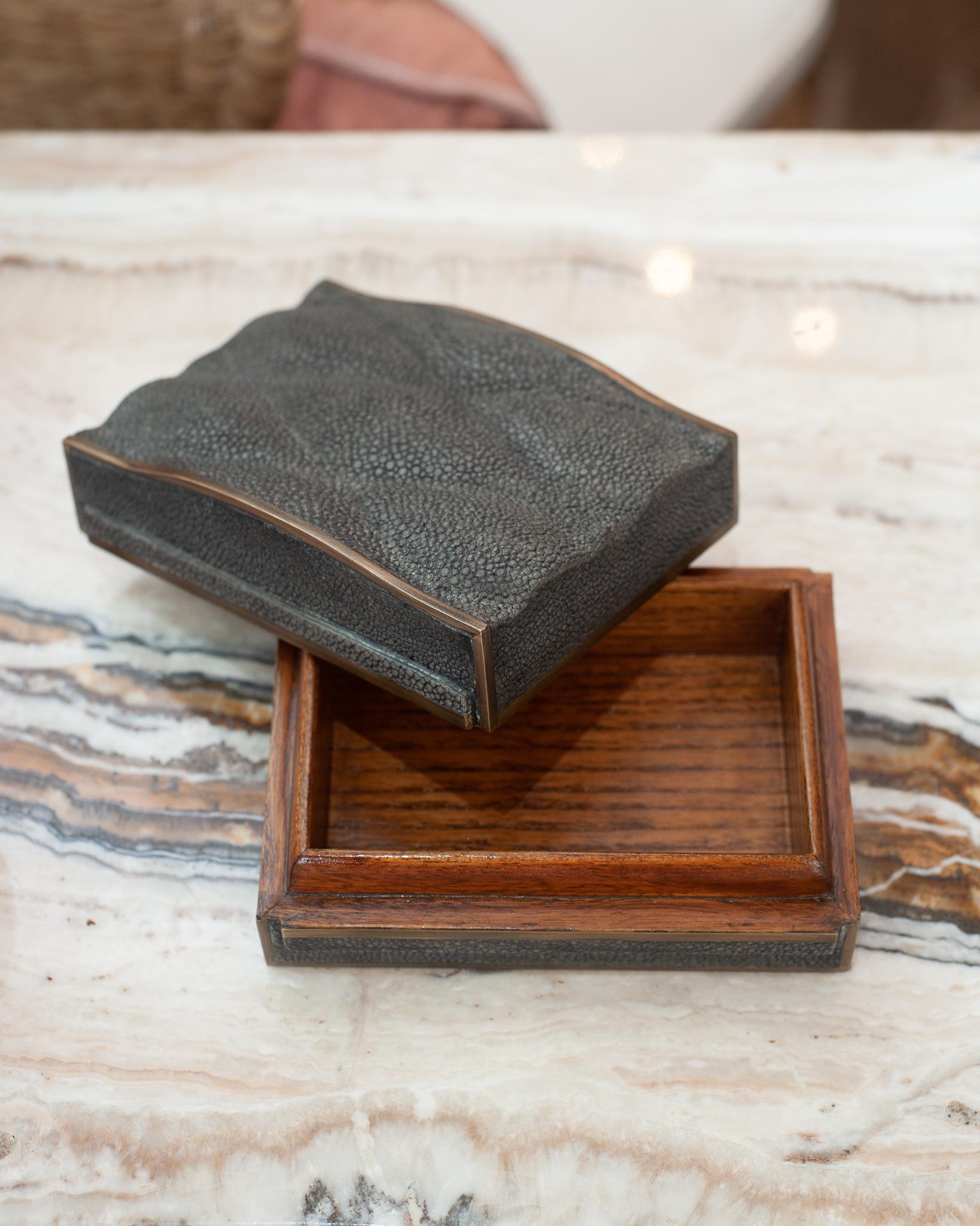 Une belle boîte matelassée en galuchat anthracite de Kifu Paris. Cette pièce en peau naturelle est entièrement réalisée à la main par des maîtres artisans pour une qualité optimale, à partir d'une base en noyer.
