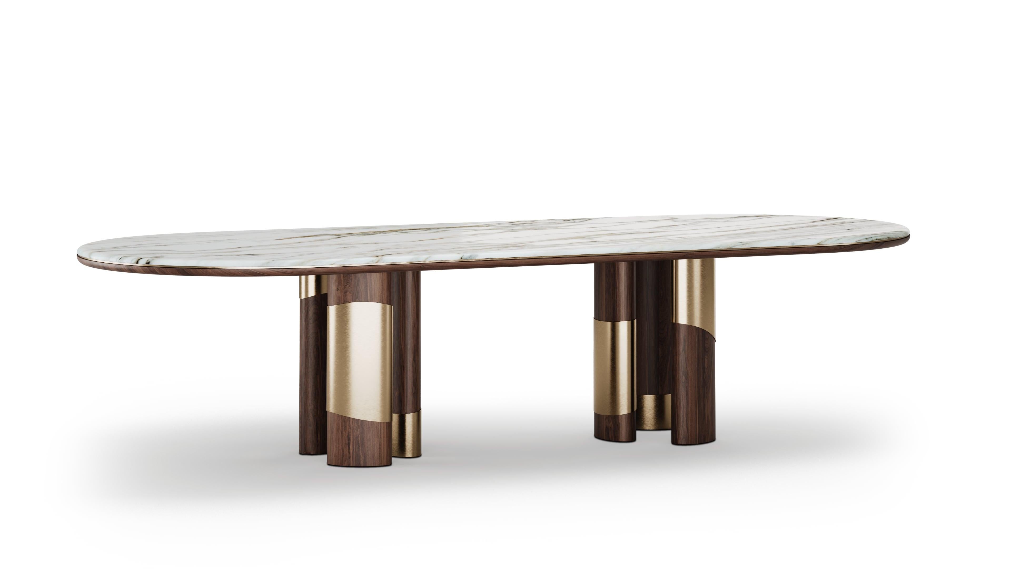 Atrevida y arquitectónica, la mesa de comedor Korin tiene un diseño sofisticado. Fabricado en rica madera de nogal, destaca el detalle de latón cepillado que rodea las patas, creando un ritmo visual escultural. La encimera de mármol Calacatta Gold
