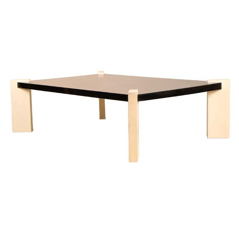 Une table basse contemporaine avec un plateau laqué noir et des pieds en peau de chèvre crème. Les pieds sont fixés en biais à chaque coin du plateau laqué, conférant un style géométrique et moderne à cette table basse chic.