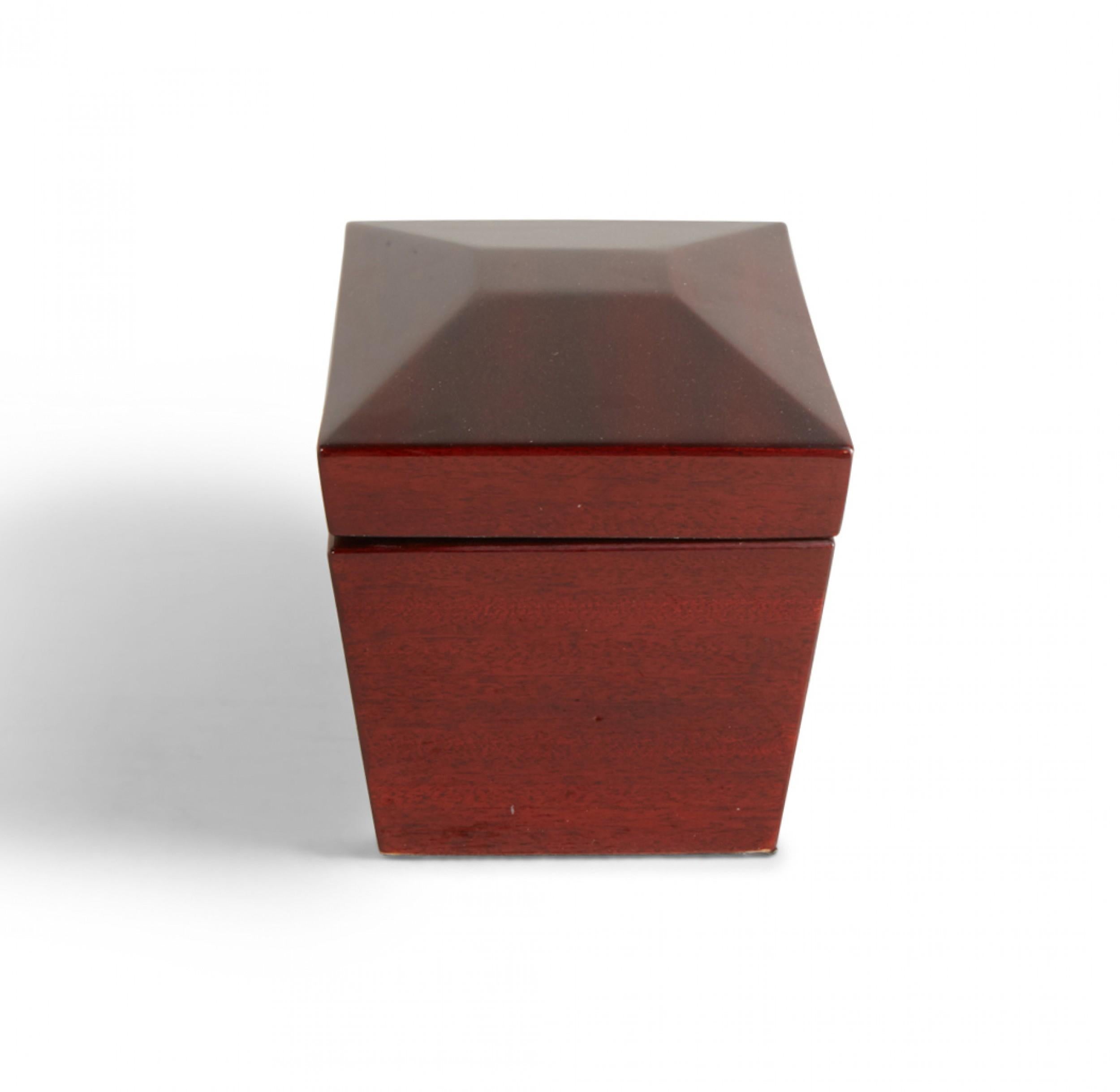 Contemporary decorative lacquered cherry wood box with a rectangular profile with faceted lid and tapered sides, and a brass-hinged lid that opens to reveal two interior compartments covered with black painted wooden square lids with turned knobs.