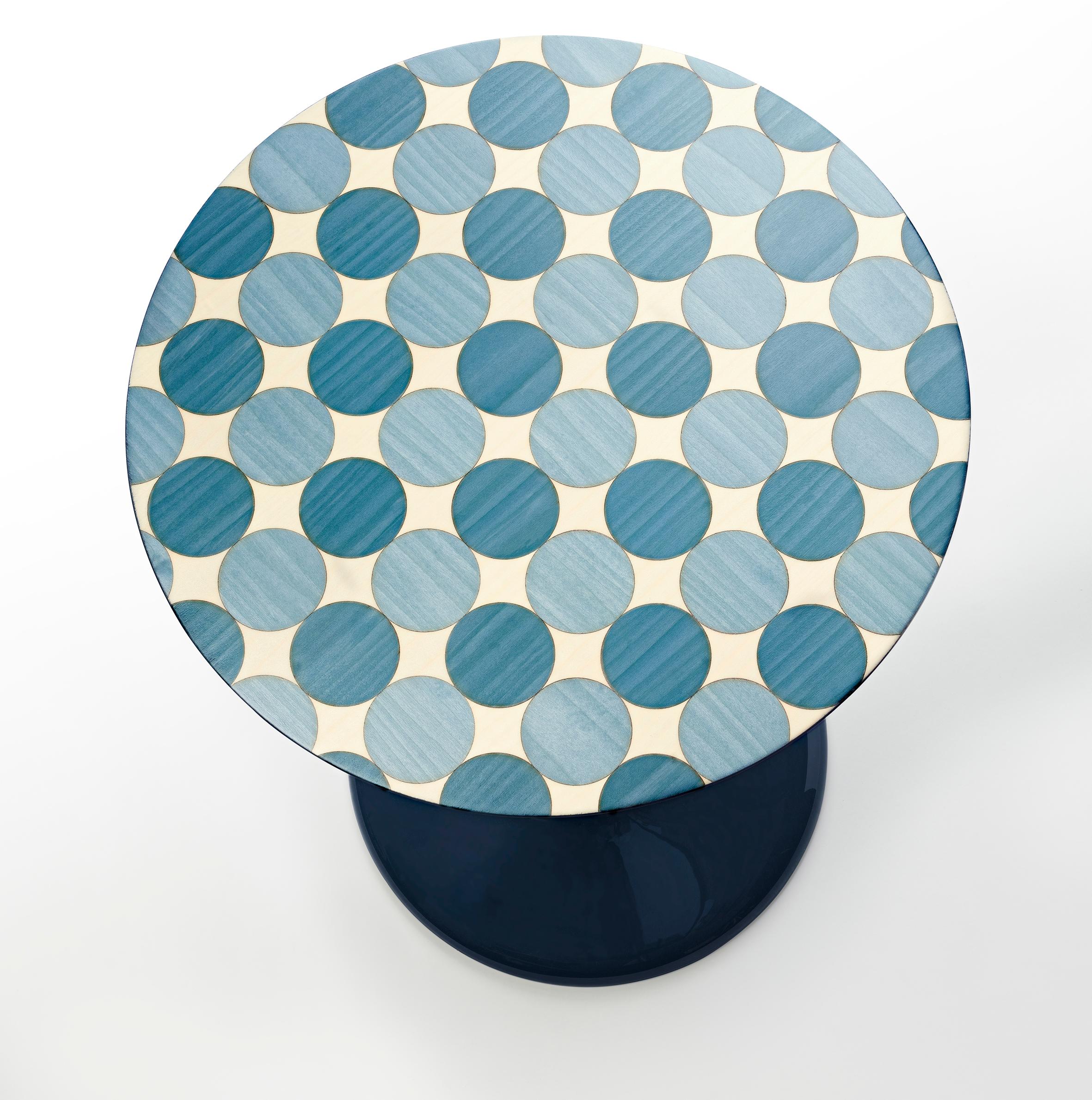 A decorative side table, entirely turned in block material and lacquered with high gloss lacquer steel blue RAL 5011. 
The top is veneered with different types of blue coloured wood representing a geometrical pattern of circles.
This table can be