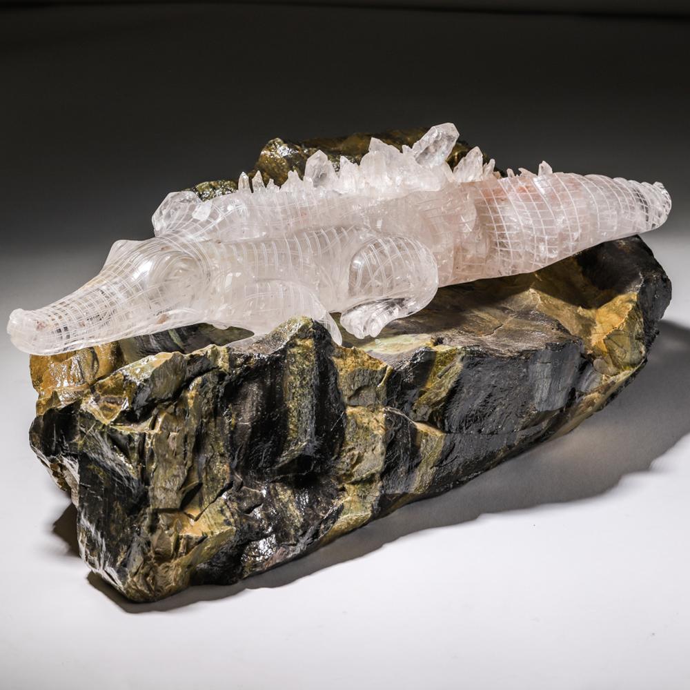 A magnificent and grand rock crystal hand carved alligator, on a large striped serpentine mineral specimen base. The alligator is finely carved from a solid piece of rock crystal, with natural crystal points lining the ridged back of the animal.
