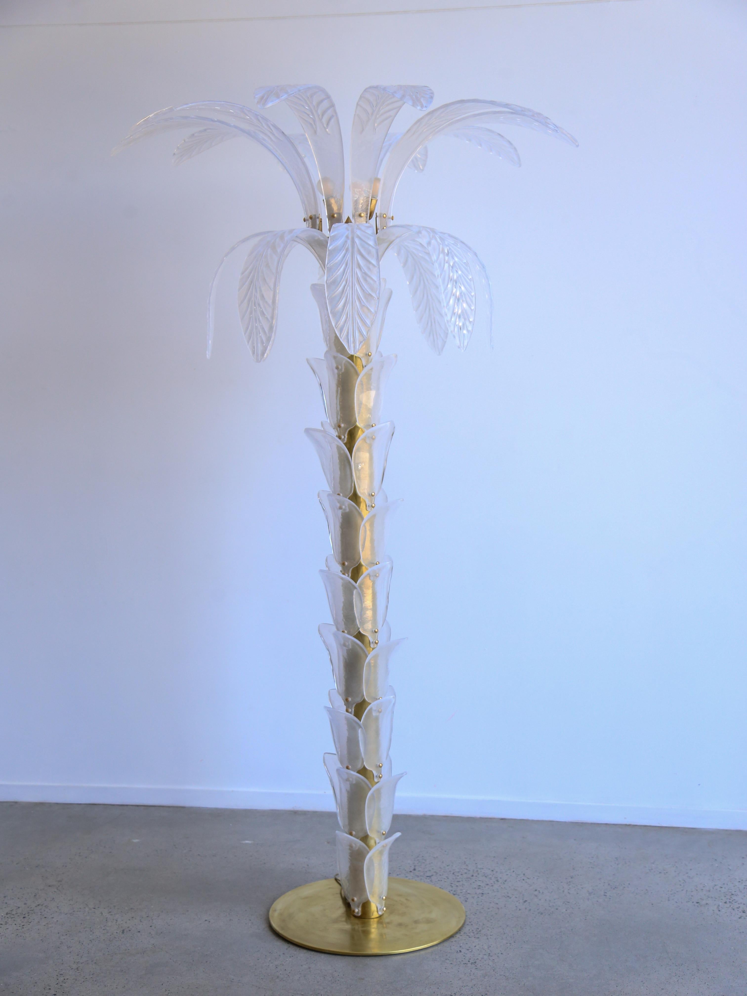 Large white-transparent floor lamp shaped like a palm tree, made of a brass circular base and trunk, covered with iridescent Murano glass leaves up to the top where large leaves burst out of the trunk, four lights inside the top section.
This is a