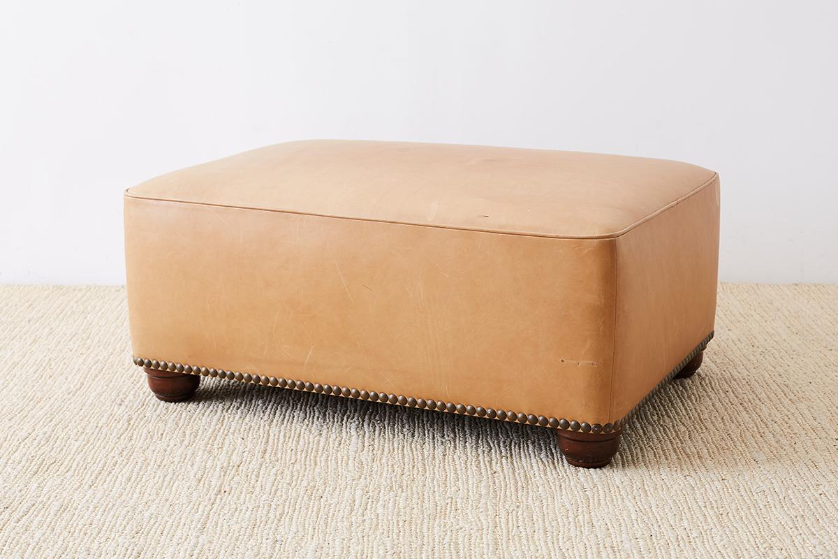 Large, rectangular ottoman or bench with a thick, natural tone leather and accented with brass nailhead trim. Contemporary style with a flat top that would also make a great coffee table for supporting large trays on top. Supported by bun style