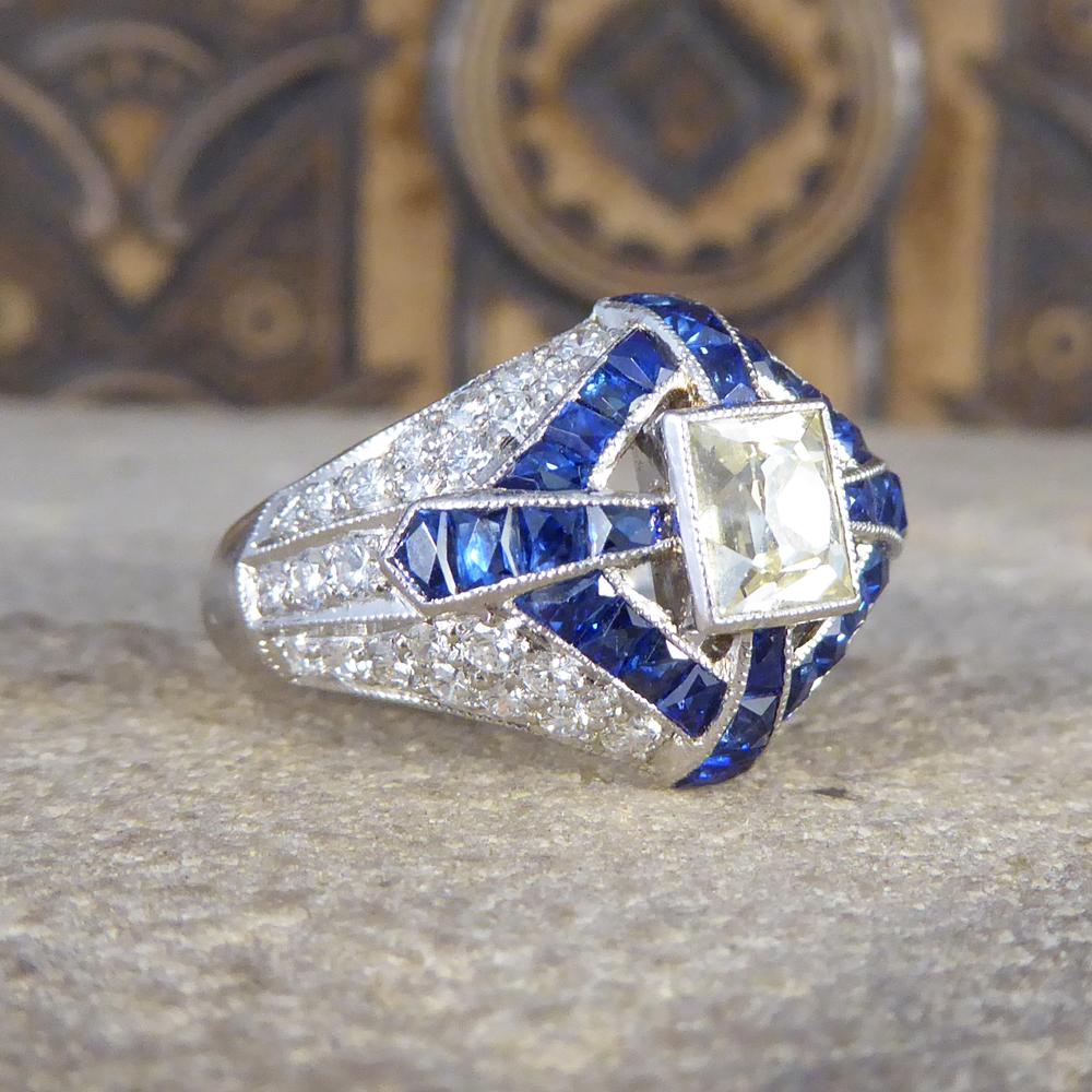 At first glance this ring shows a cross running through the face of this ring in French Cut Sapphires leading down to Diamond set shoulders. It features and elongated French Cut Diamond in the centre to be described as Lemon tinted, emphasised this