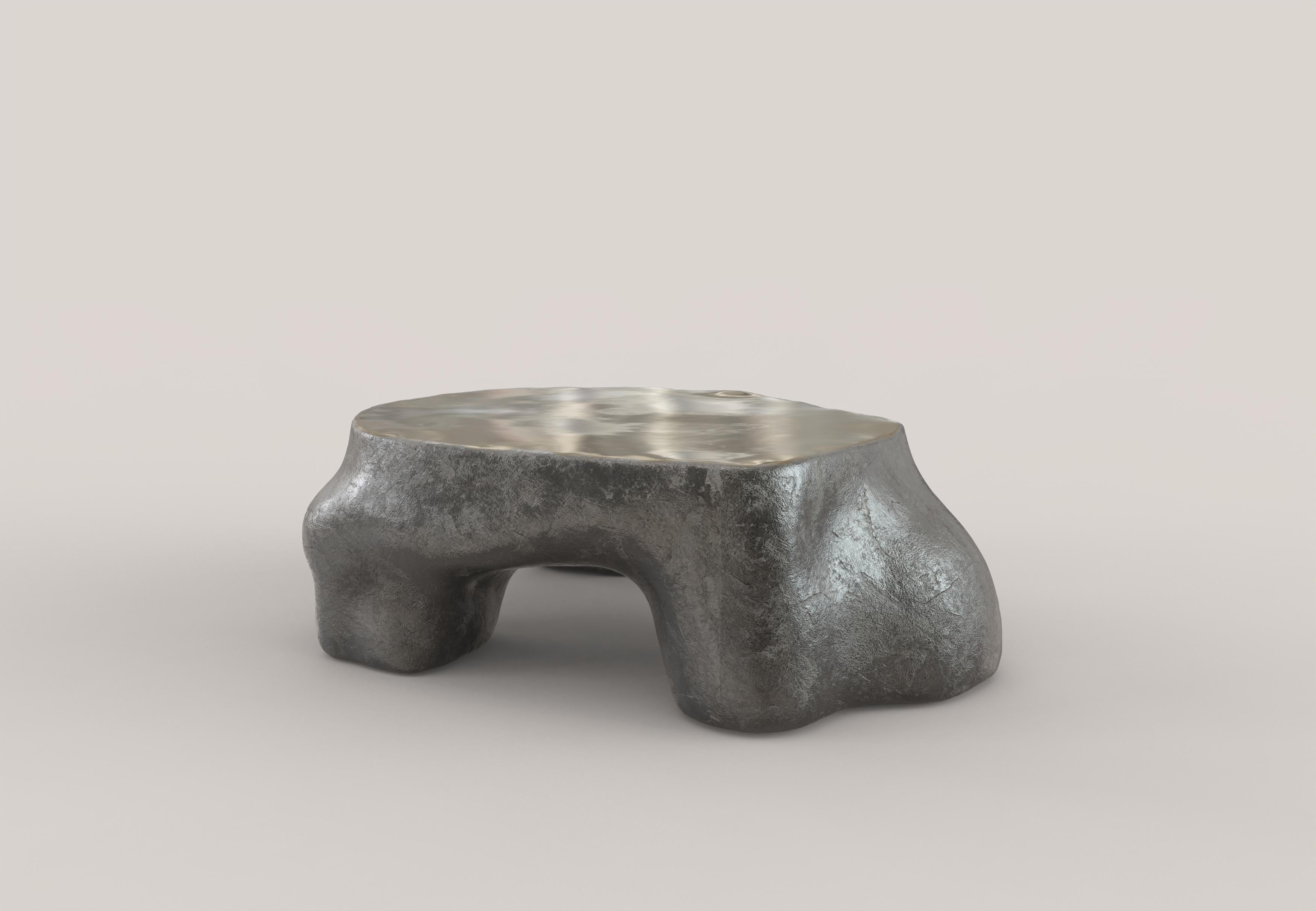 A sculptural low table made of patinated and polished cast bronze. The shapes of the table and the patina on the body of the piece recall natural architecture, constructions born of an organic matter in motion, growing. The clean-cut and