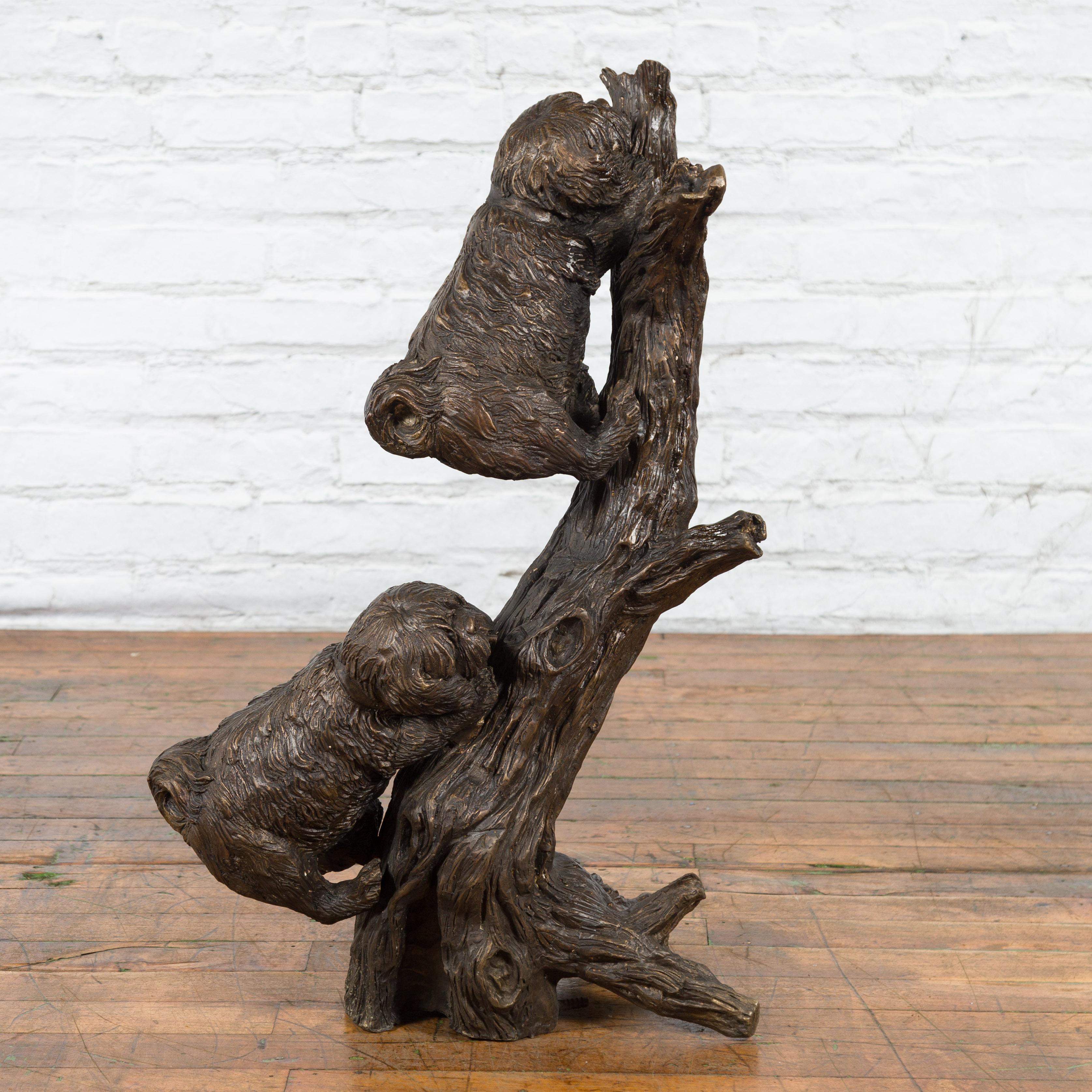 Eine zeitgenössische, in Wachsausschmelzverfahren gegossene Bronzeskulptur, die zwei Hunde darstellt, die auf einen Baum klettern, mit von Hand aufgetragener Bronzepatina. Diese skurrile Skulptur wurde mit der traditionellen Technik des verlorenen