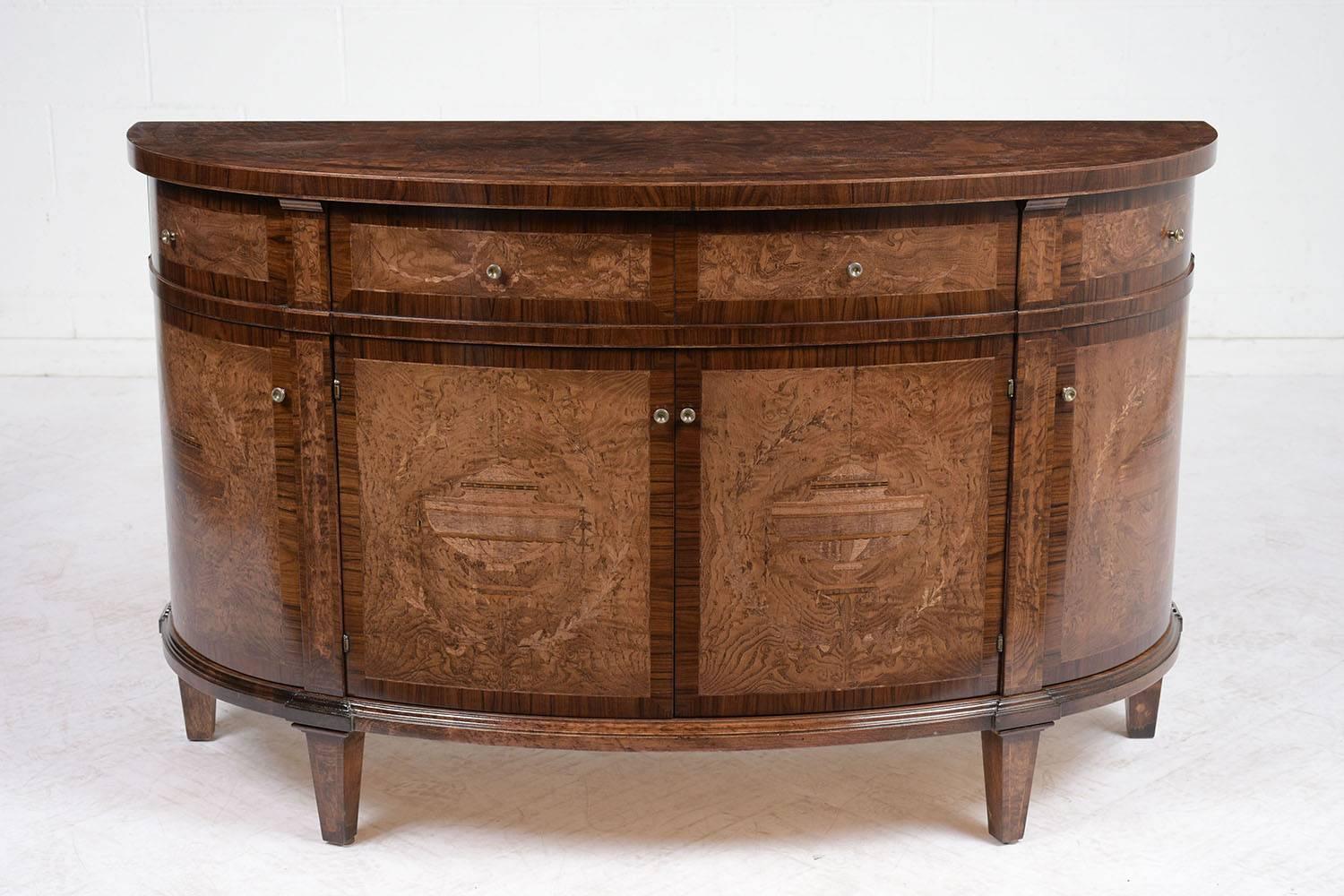 This 2000's Louis XVI-style demilune buffet is adorned with ornate marquetry and inlaid details stained in a walnut color with a lacquered finish. The veneers covering the buffet depict garden urns surrounded by leafy garlands and floral accents.