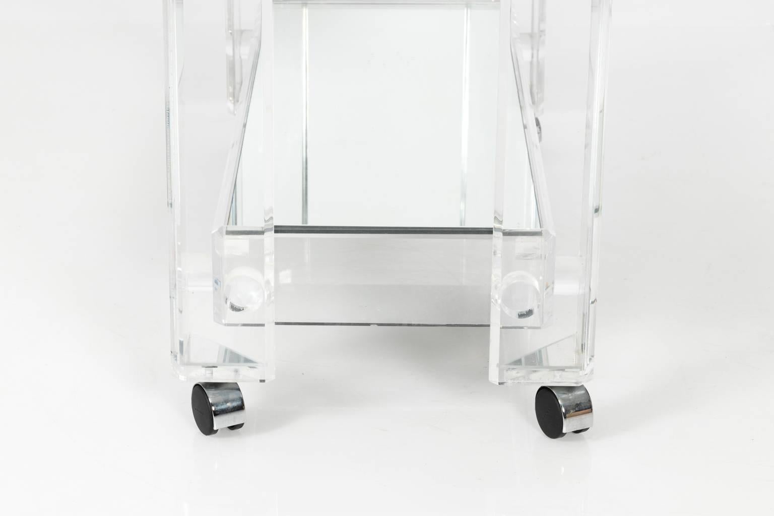 Contemporary Lucite bar cart with two mirrored shelves on wheels.
 