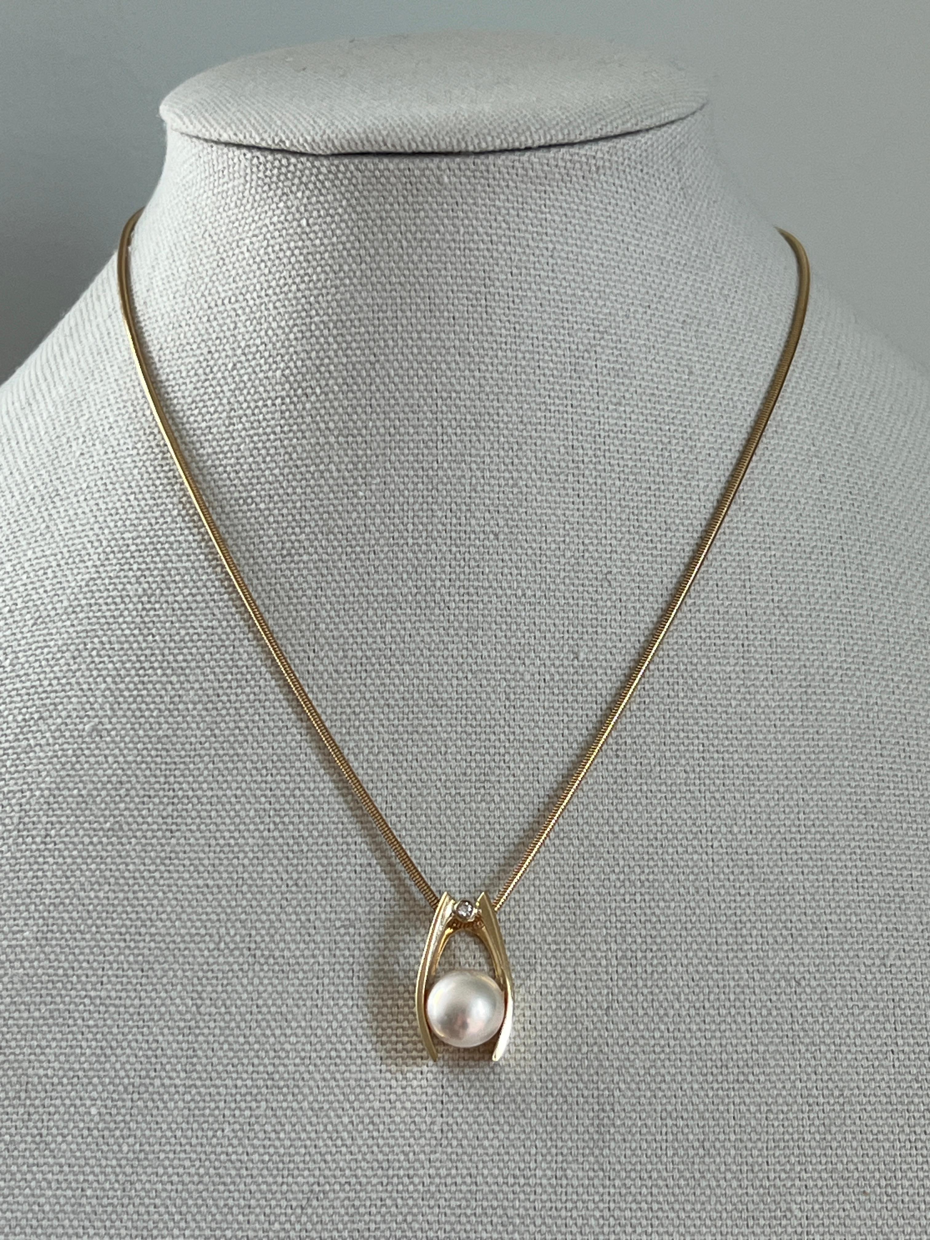 This contemporary 14 karat yellow gold wishbone-style pendant beautifully showcases an 11.8mm Mabe pearl, complemented by a 0.03-carat round brilliant diamond with G color and SI2 clarity. Measuring 1.02 x 0.57 inches, the pendant has a 4.8mm bail