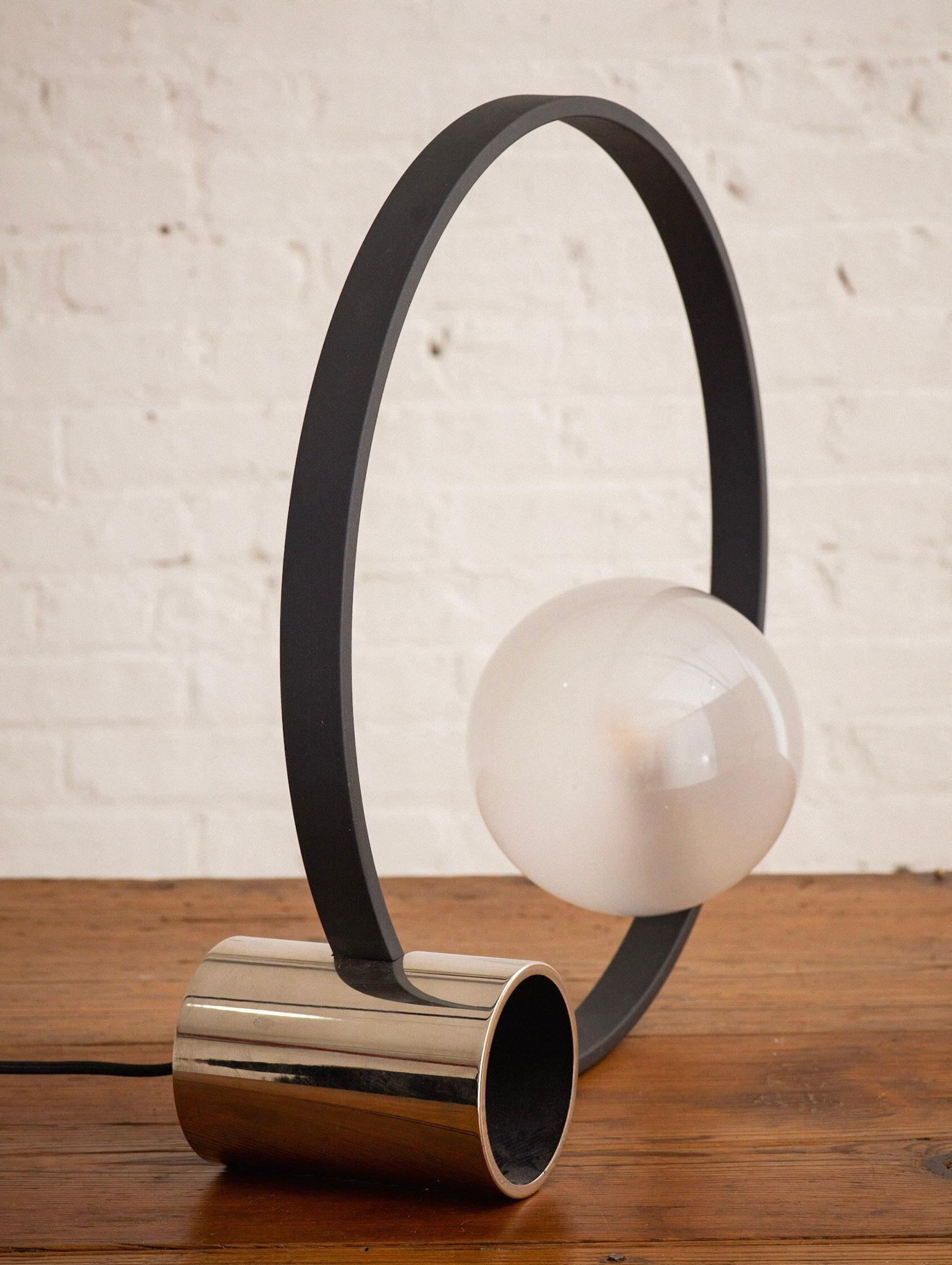 A Memphis style sculptural lamp in glass, metal and chrome. A chrome base supports a round metal frame and glass glove. Marked Ul LLC 2013.