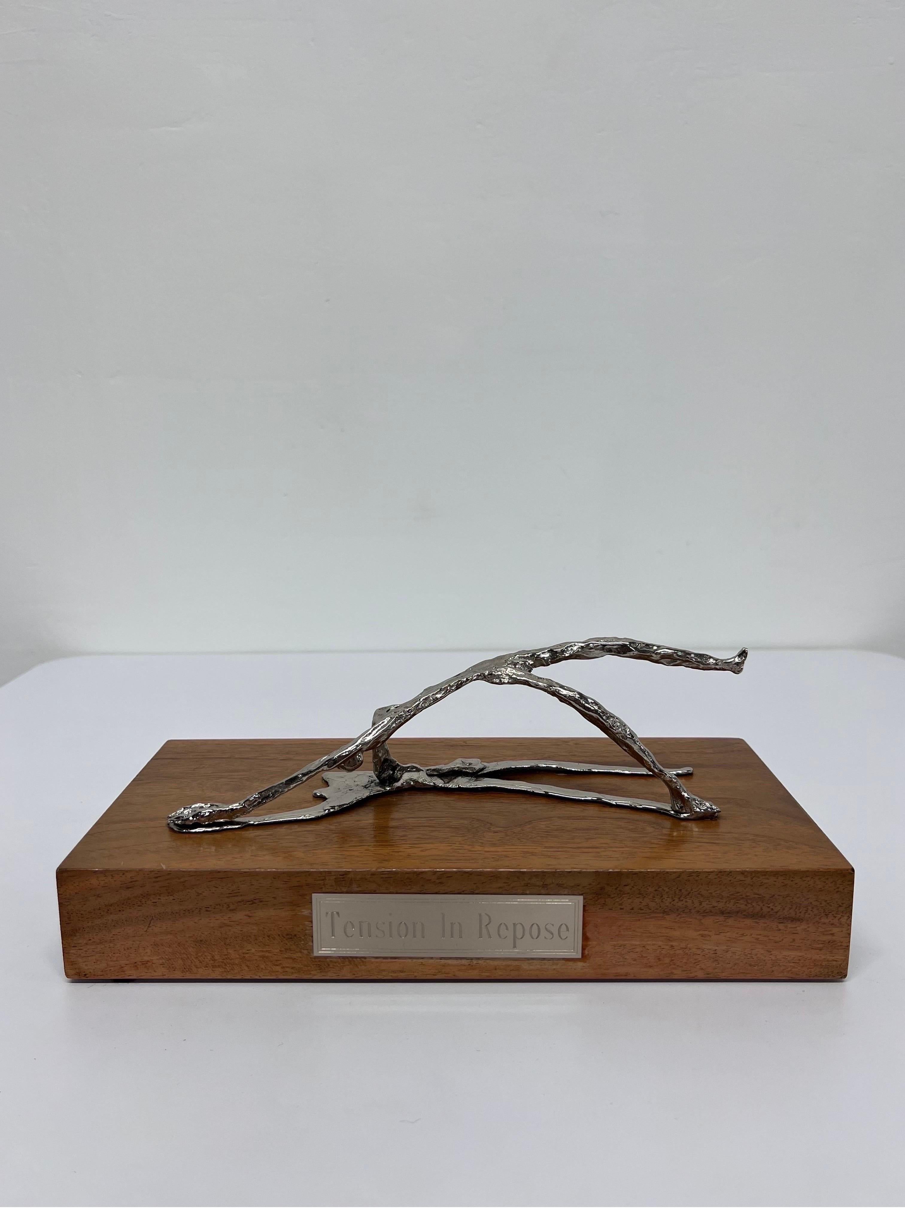Sculptural polished steel figure on wood base titled Tension in Repose.