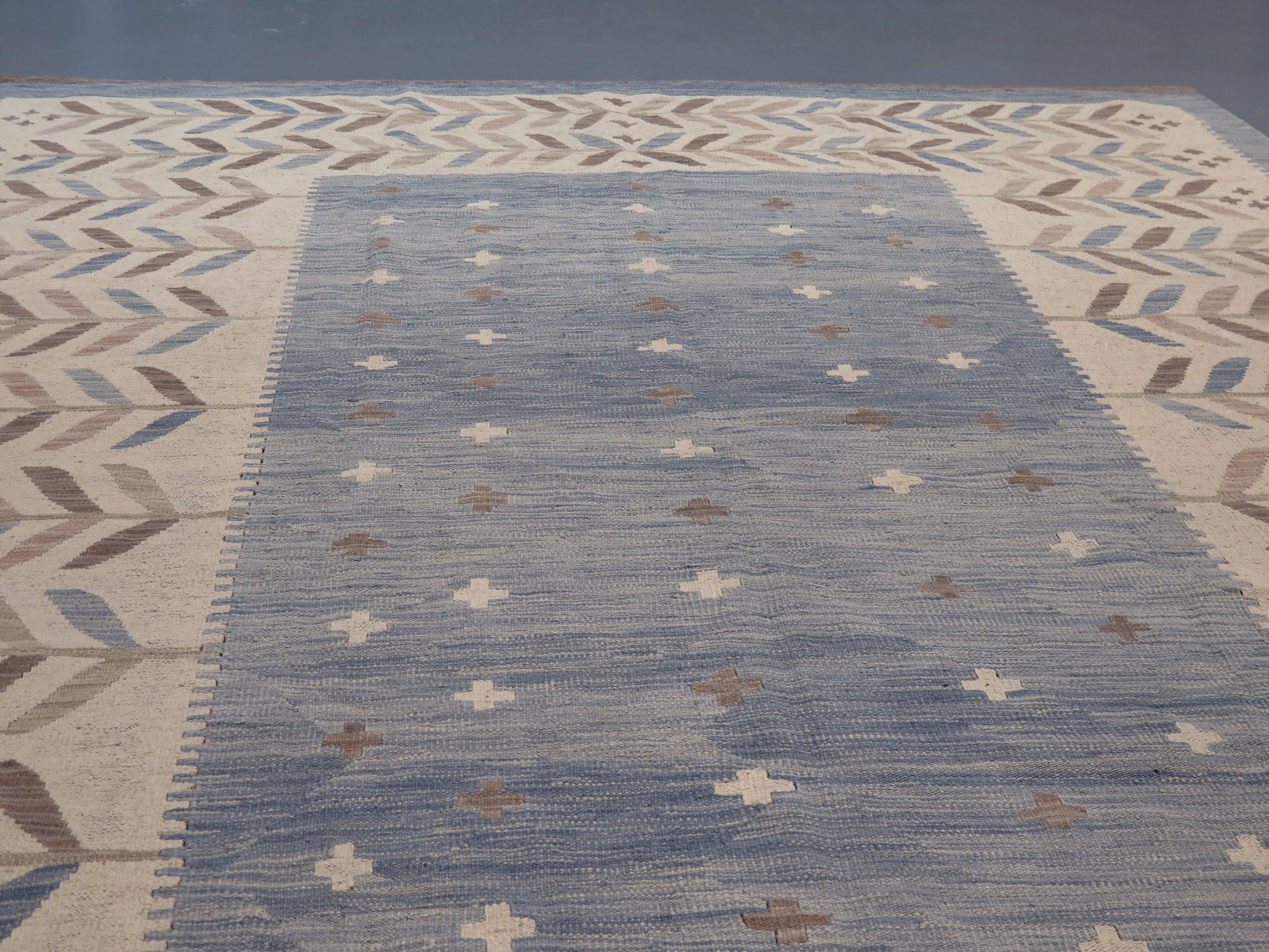 Un tapis contemporain épuré, tissé à plat, inspiré par le design suédois moderne du milieu du siècle dernier. Le champ va du bleu de Prusse à l'aigue-marine, donnant une impression de richesse et de profondeur à sa composition, par ailleurs sobre et