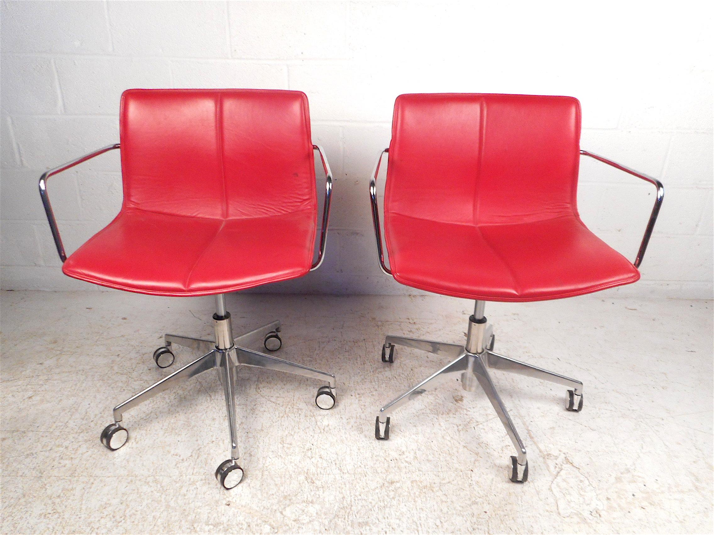 Stylish pair of modern chairs. Comfortable form-fitting seats covered in a vibrant red faux-leather upholstery. Sturdy chrome supports, bases, and armrests. Adjustable height settings ranging from 35