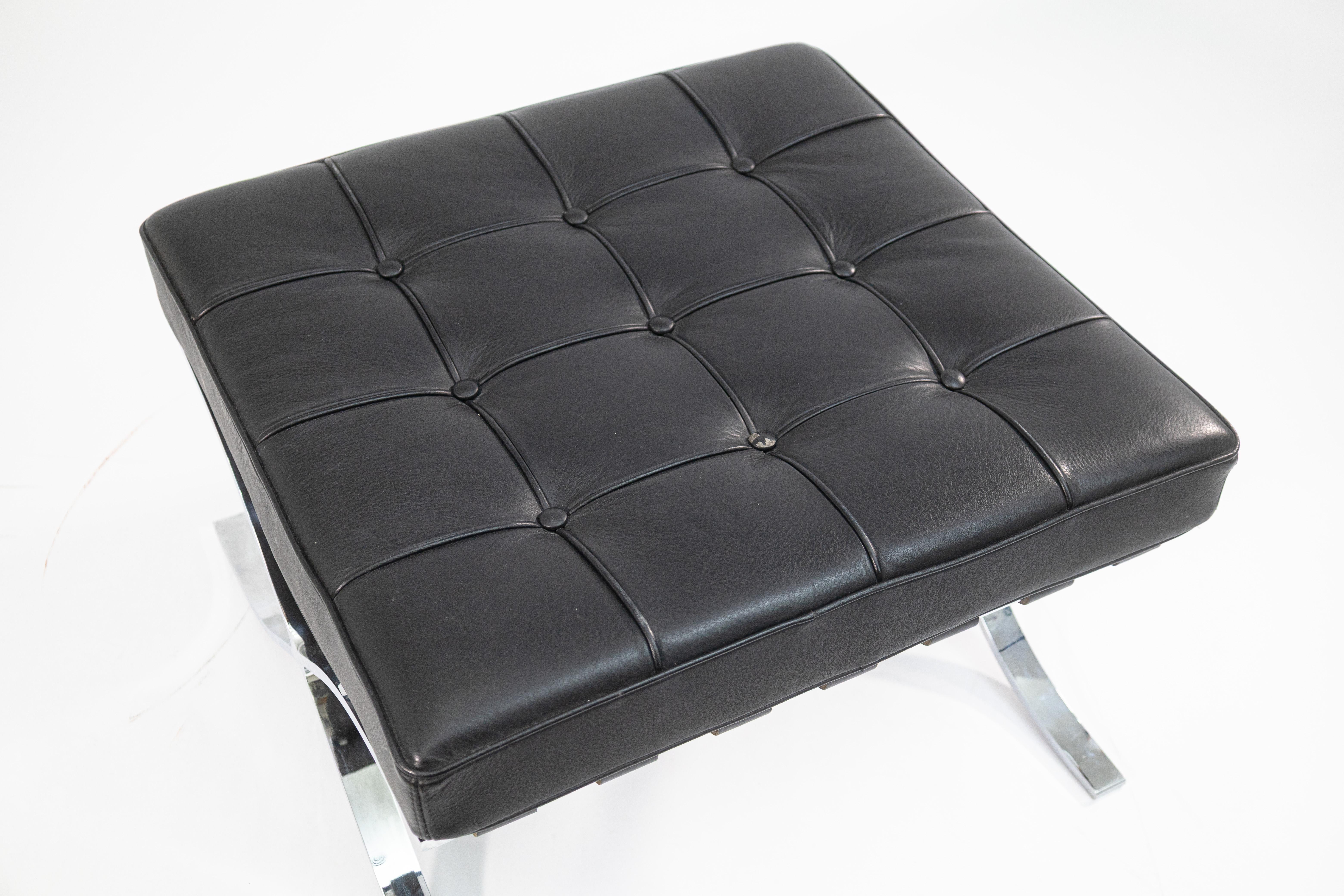 Un pouf in stile Barcellona di Mies Van Der Rohe. Questo fantastico pouf moderno contemporaneo presenta un design classico della metà del secolo scorso. Presenta un cuscino in pelle nera completamente trapuntato, appoggiato su cinghie di pelle nella