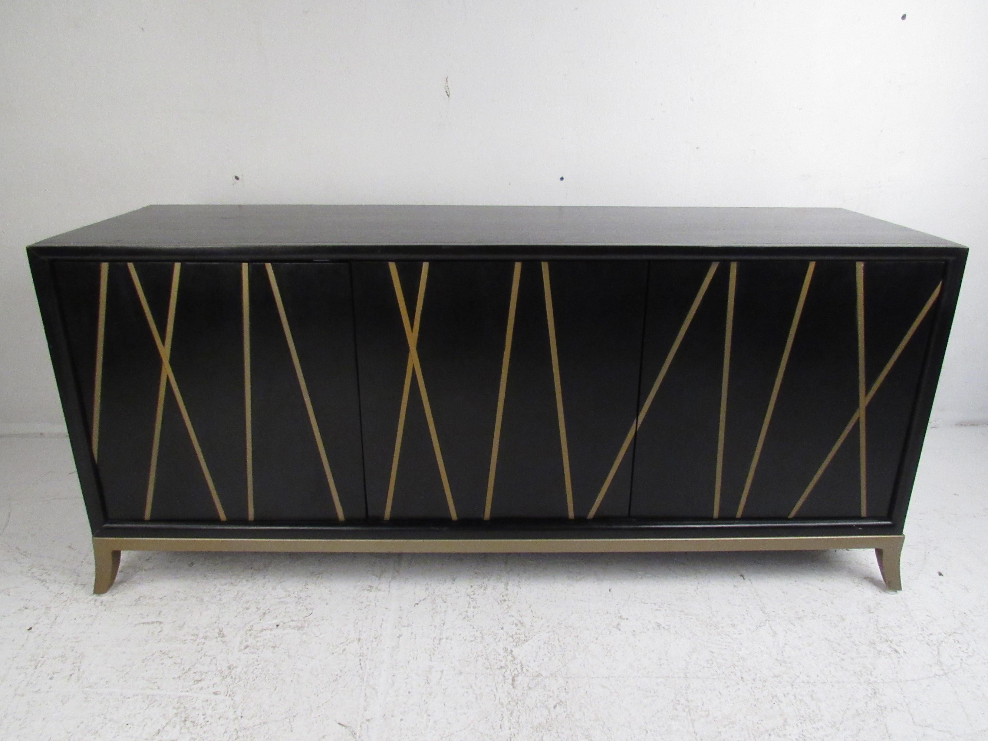This sleek contemporary modern buffet features a two-tone design painted black with slightly embossed gold/brass colored lines on the front. A functional and stylish case piece with two cabinet doors that open to unveil a large storage compartment.