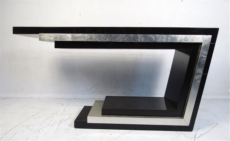 This beautiful midcentury style console table features a cantilever two-tone design. The sleek shape allows this versatile piece to function in any home, business, or office. The unique angled side and black tile-like top add to the allure. This