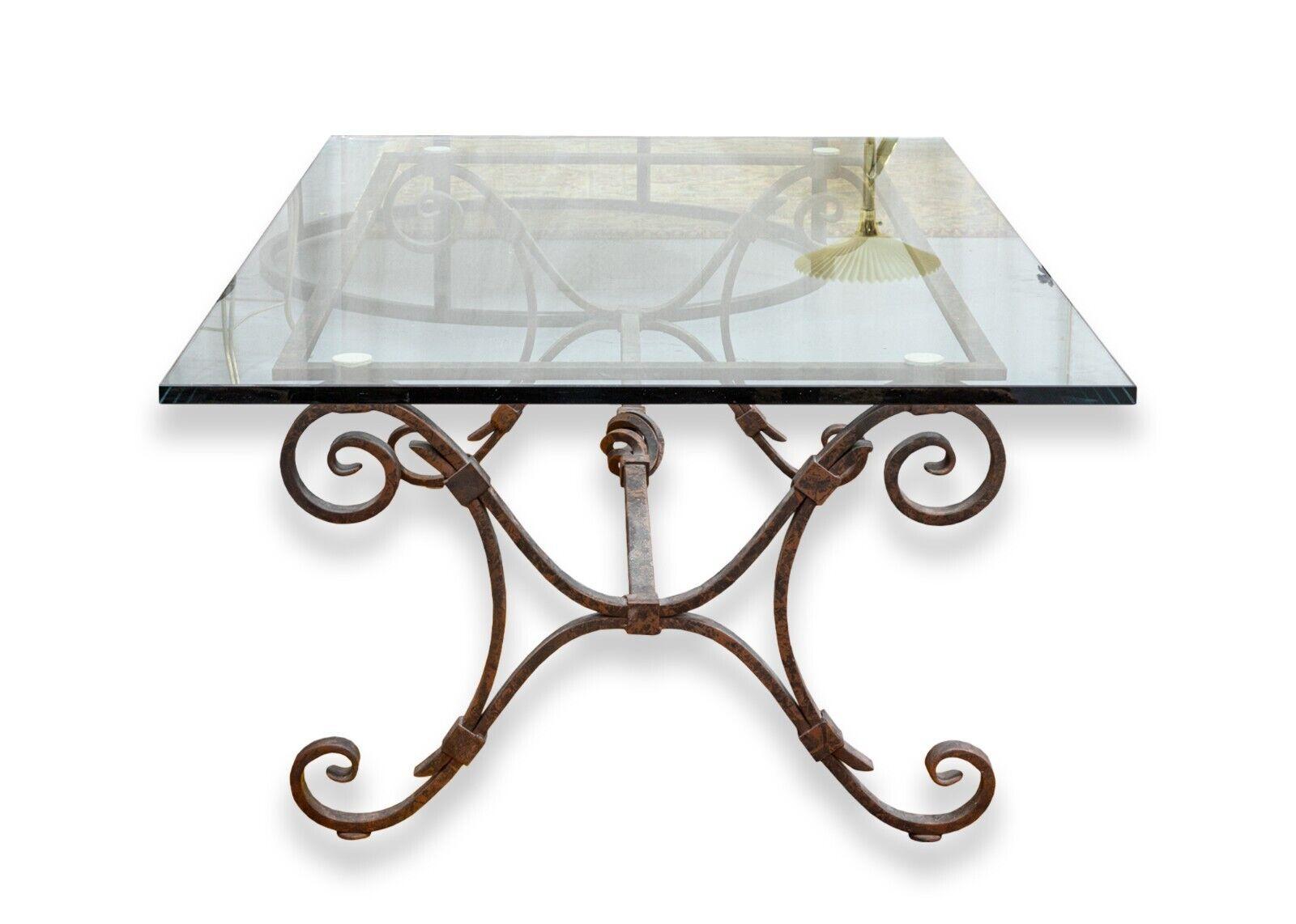 A contemporary modern iron and glass rectangular coffee table. This beautiful coffee table features an ornate iron base design with curving and swirling iron details. The table top is a thick piece of clear glass, resting on soft touch corner pads.