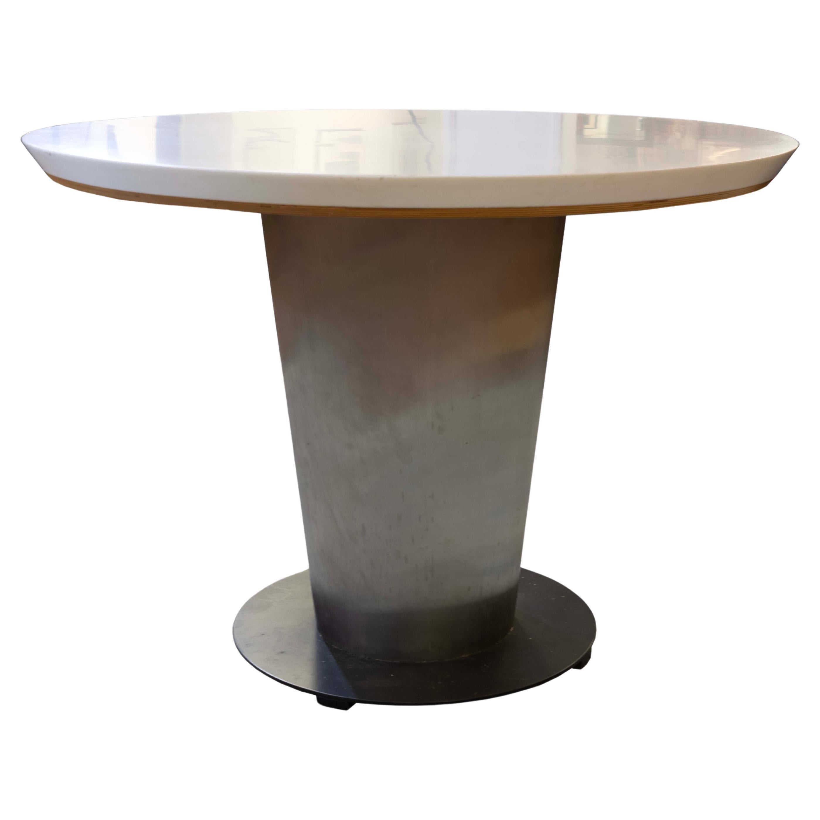 This contemporary modern dinette table features a sturdy metal pedestal base with a sleek, round laminate top. The table's design combines functionality with a minimalist aesthetic, highlighted by the contrast between the metallic finish of the base