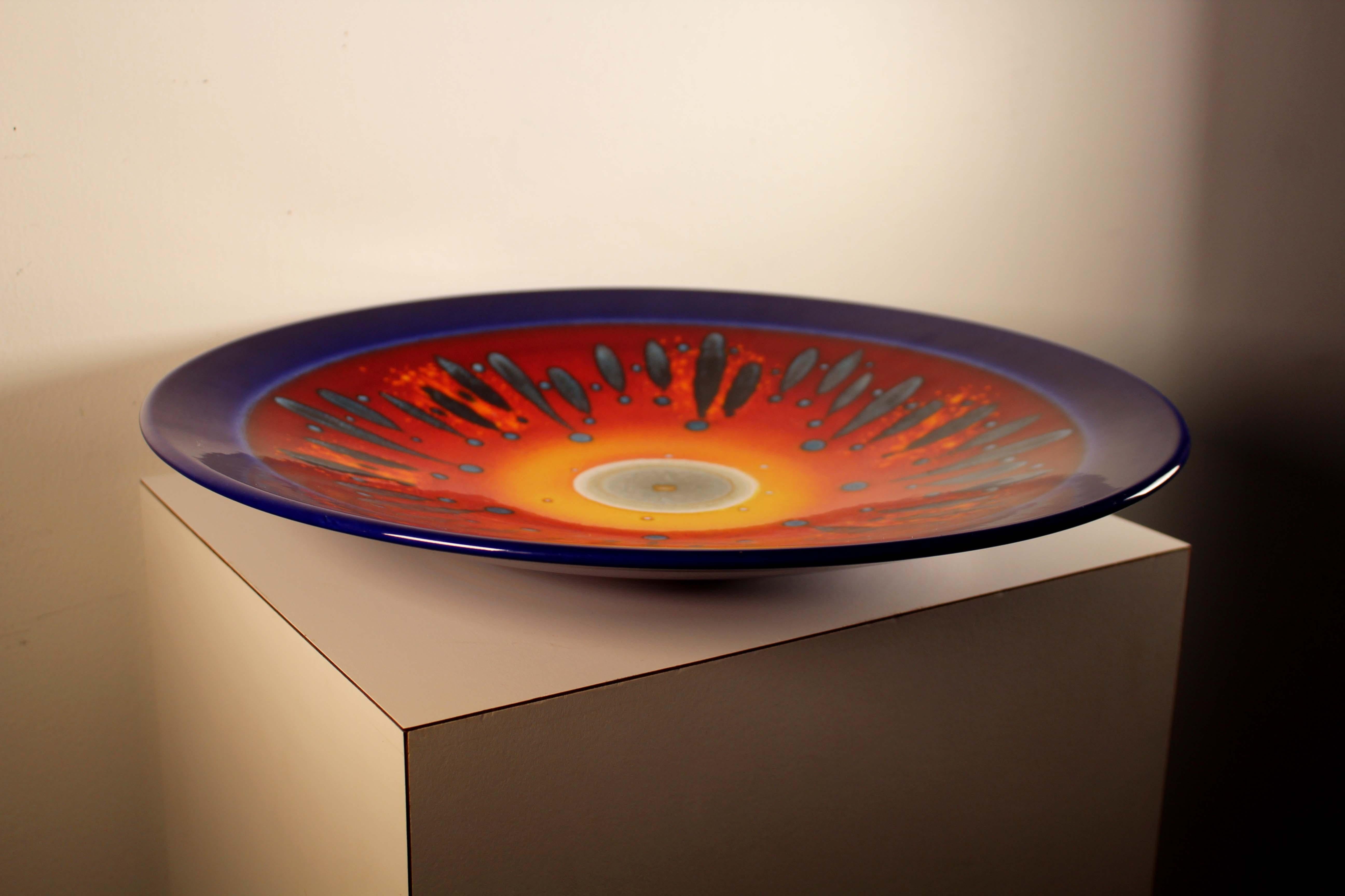 A Poole Pottery 'Third Millennium' pattern charger by Alan Clarke, decorated with an abstract design in yellow, orange and red against a dark blue ground, printed factory mark and blue painted signature to base. Dimensions: 16
