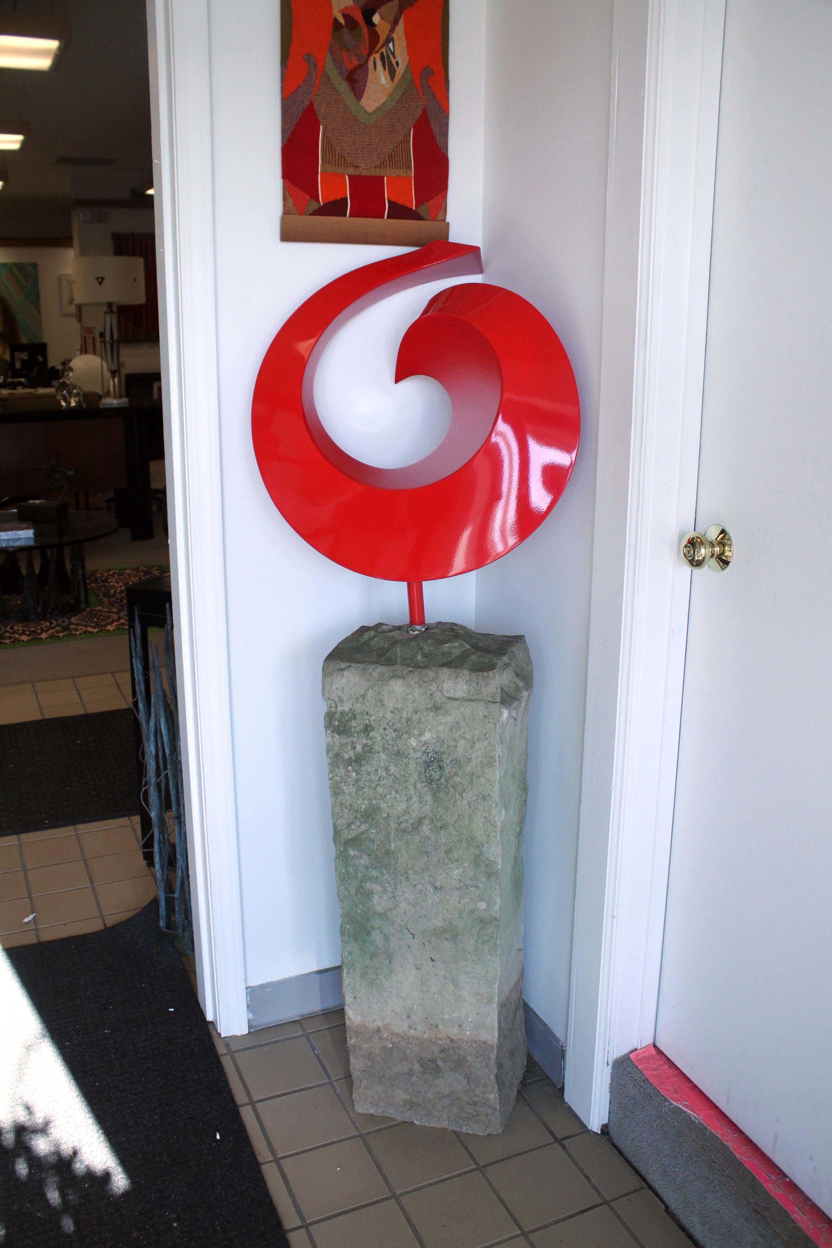 For your consideration is this striking statement piece of a sculpture with an abstract red metal circular swirl, mounted atop a stone pedestal base. Dimensions: 21.5