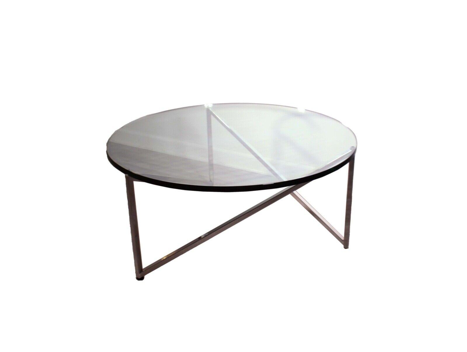 This contemporary round glass top coffee table features a stainless steel base with a sleek, modern design attributed to Breuton. The thick glass top provides a sturdy and eye-catching surface that is sure to be a conversation starter. The stainless