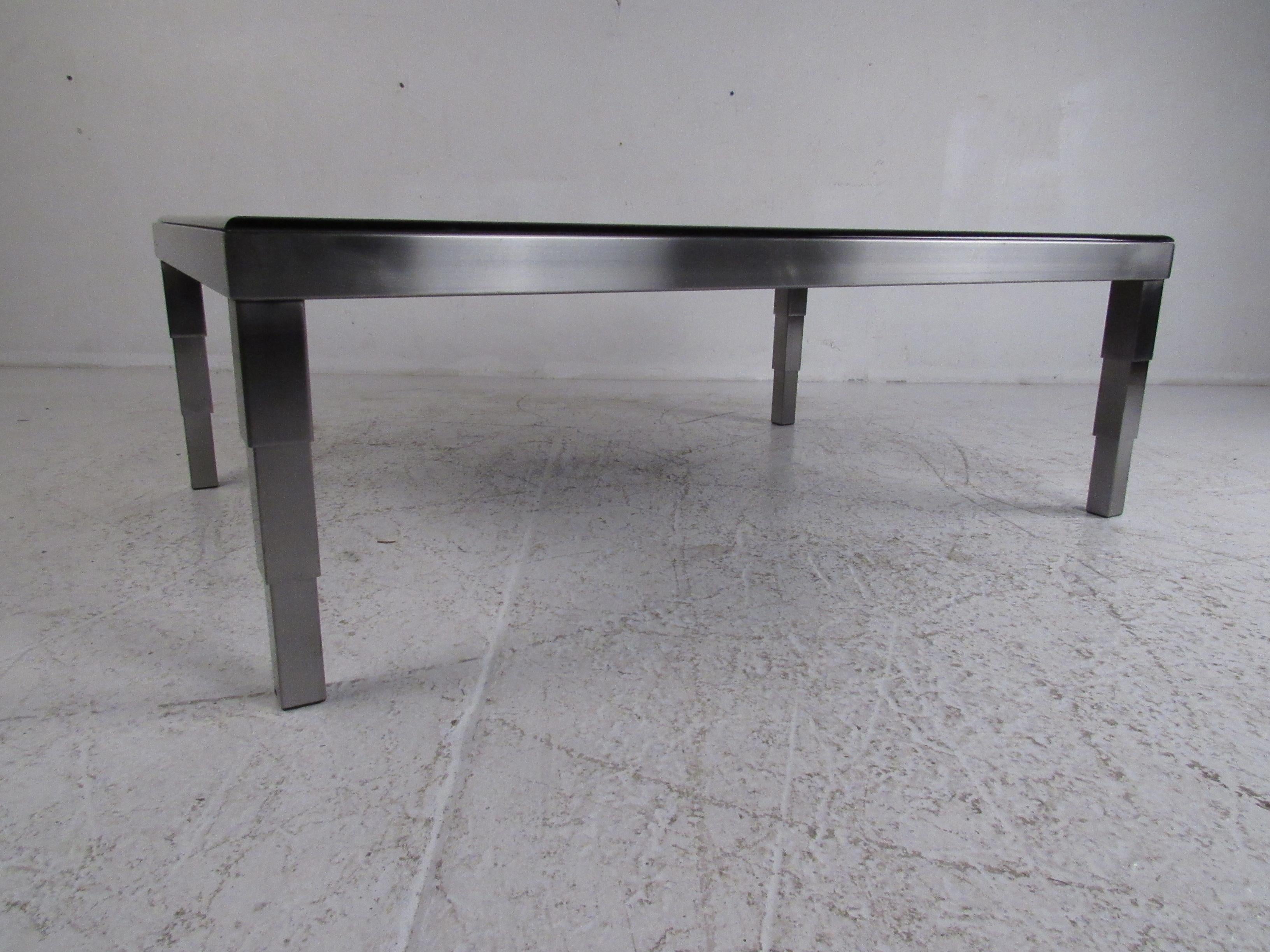 This stunning vintage modern coffee table boasts a stainless steel base with unique legs that graduate downward. A smoked rectangular piece of glass with beveled edges sits comfortably on top. This stylish retro style coffee table makes the perfect