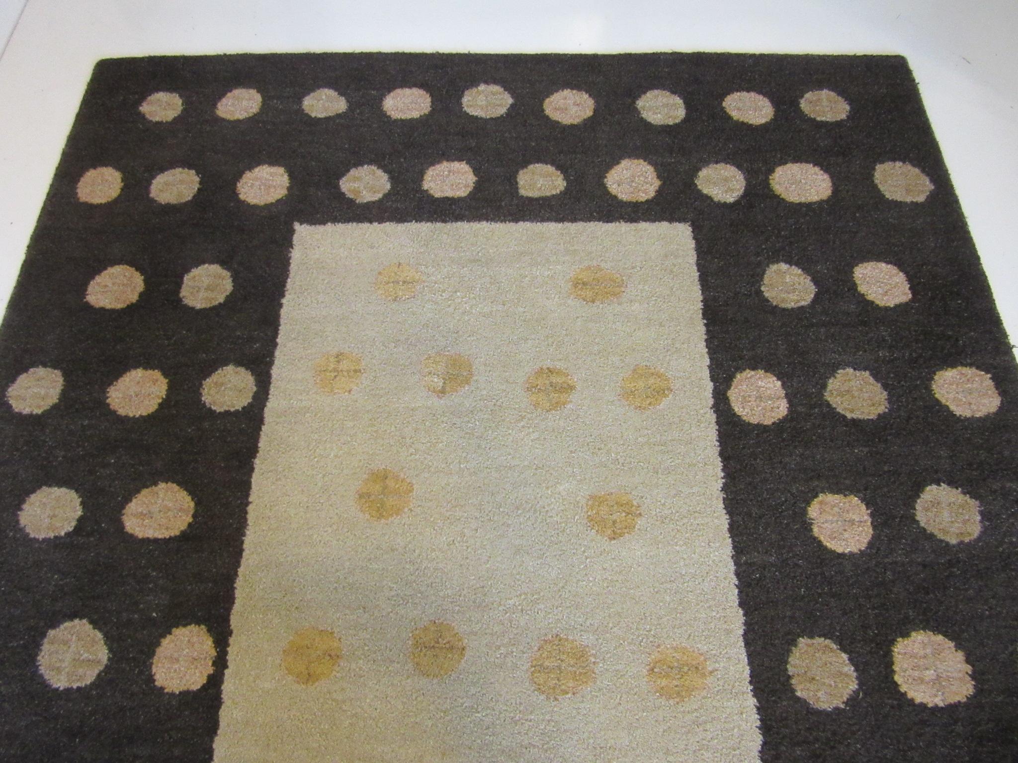 A low cut pile 100% wool contemporary styled designer rug with dark brown, tan, taupe colors having dot and X designs. This rug has a linen backing and serged edges, well crafted and heavy perfect for that room that needs some understated pop.