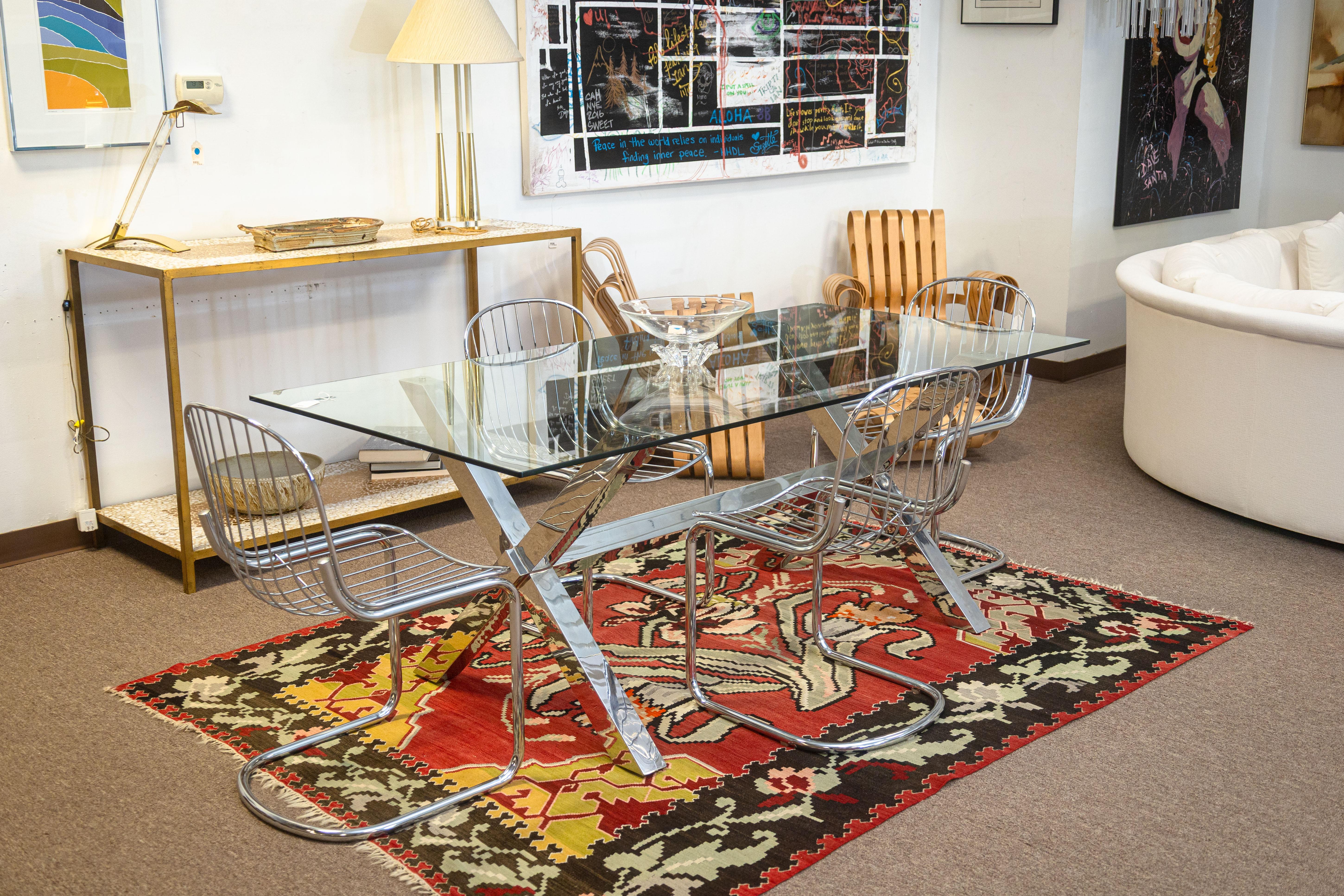 A contemporary modern chrome and glass dining room table. This is a lovely, chic dining room table featuring a large rectangular glass table top and a large chrome base. The polished chrome base features two X-shaped legs with a connecting beam.