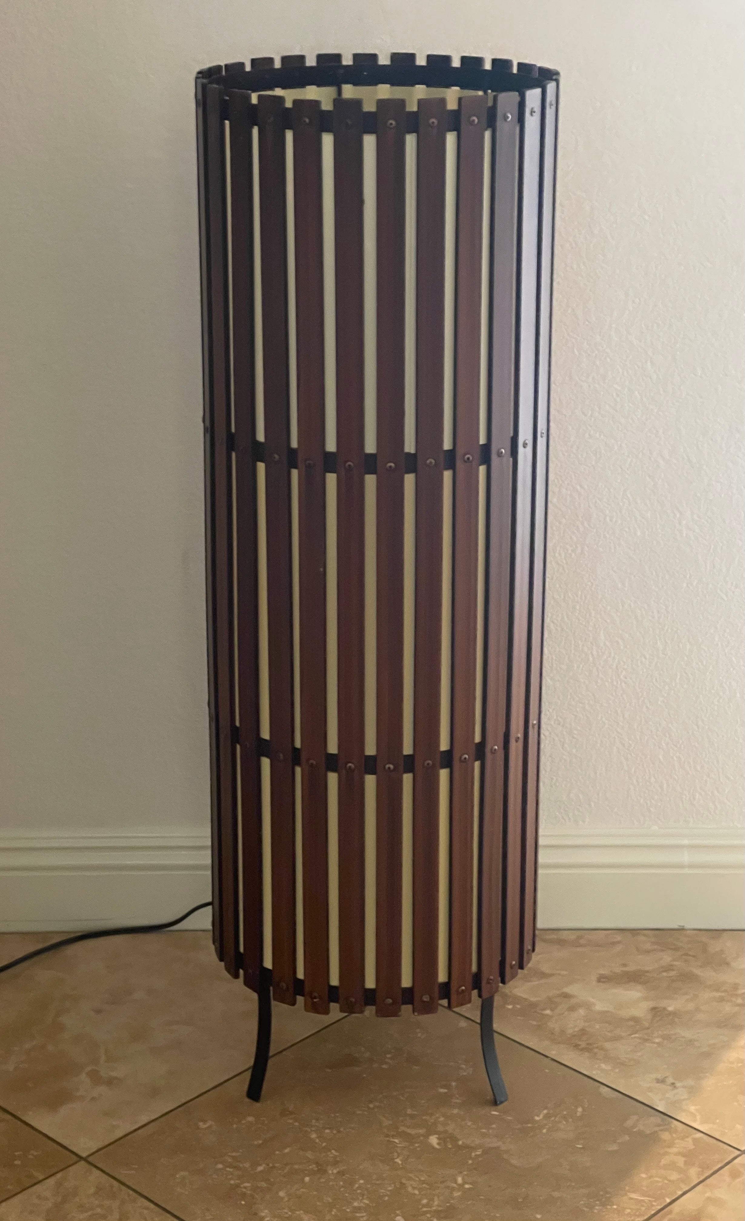 A very hard to find contemporary modernist walnut slat cylindrical floor lamp, circa 1970s. The lamp is made of solid walnut slats surrounding a white acrylic cylinder shaped shade on black metal feet. Wonderful warm glow when illuminated; the piece