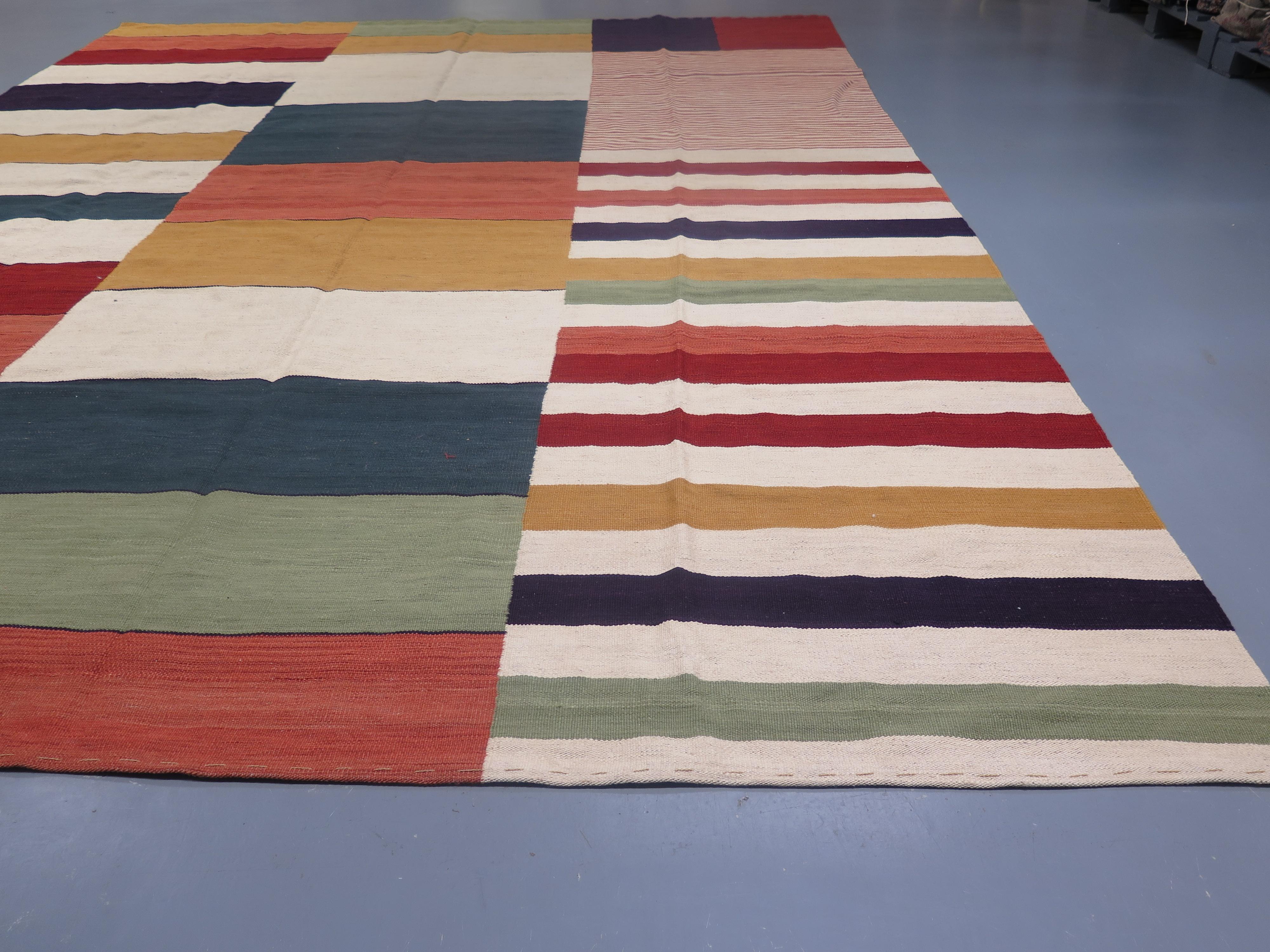 Ce Kilim contemporain intéressant, inspiré par les pièces modernes du milieu du XXe siècle, présente une série de bandes irrégulières répétées de manière créative sur le champ dans une gamme de couleurs chaudes teintées dans la masse. L'abrash