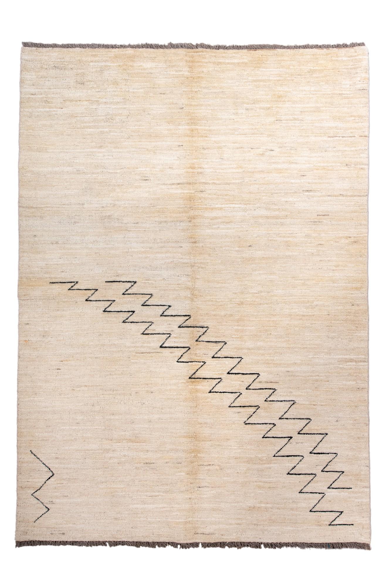 Dieser moderne Teppich im Berberstil zeigt ein minimalistisches cremefarbenes Feld, das von einer kühnen Zickzacklinie aus dunkler Wolle durchbrochen wird. Die offene Komposition und die subtilen Farbtonvariationen verleihen dem Stück eine ruhige,