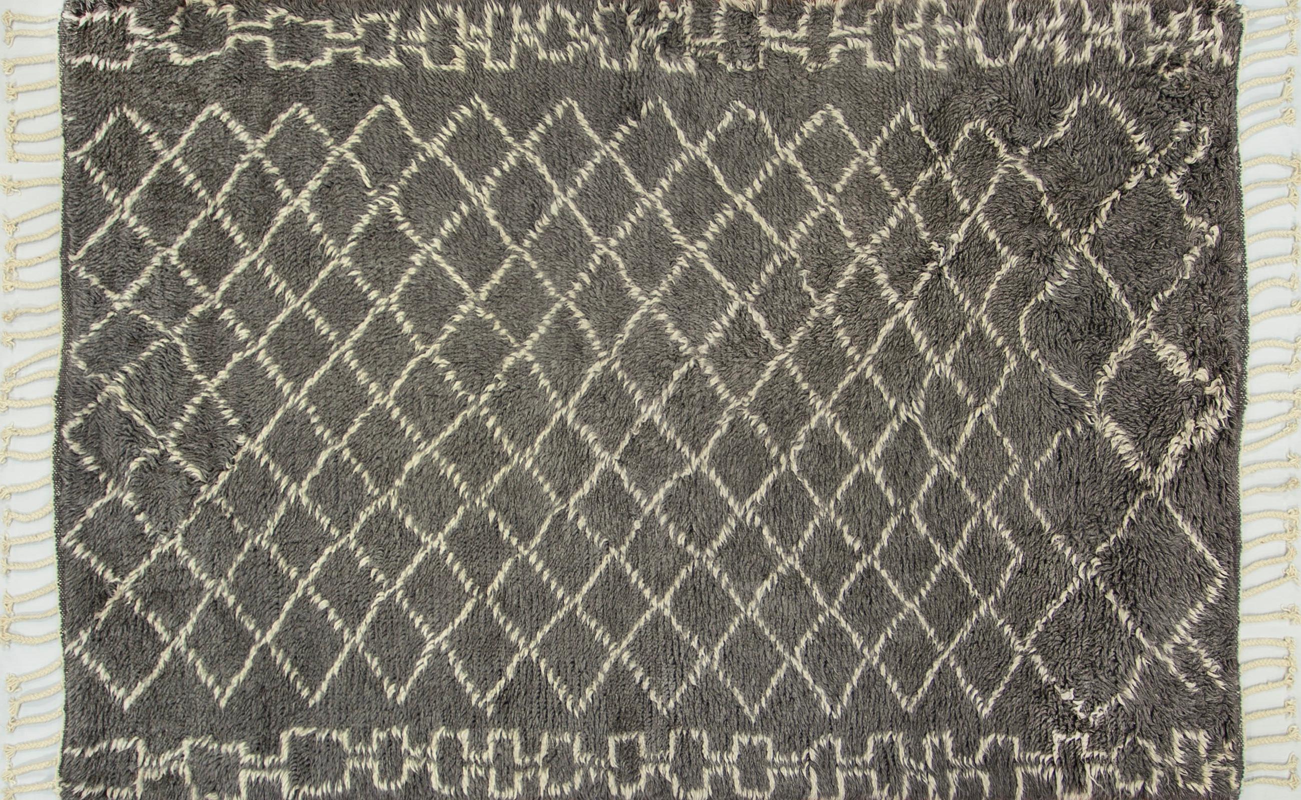 This modern Moroccan style gray rug features a geometric lattice design of ivory on a two inch plush gray ground bound with ivory fringes on the two short ends. This highly durable rug is hand knotted from the finest wool fibers with minimally