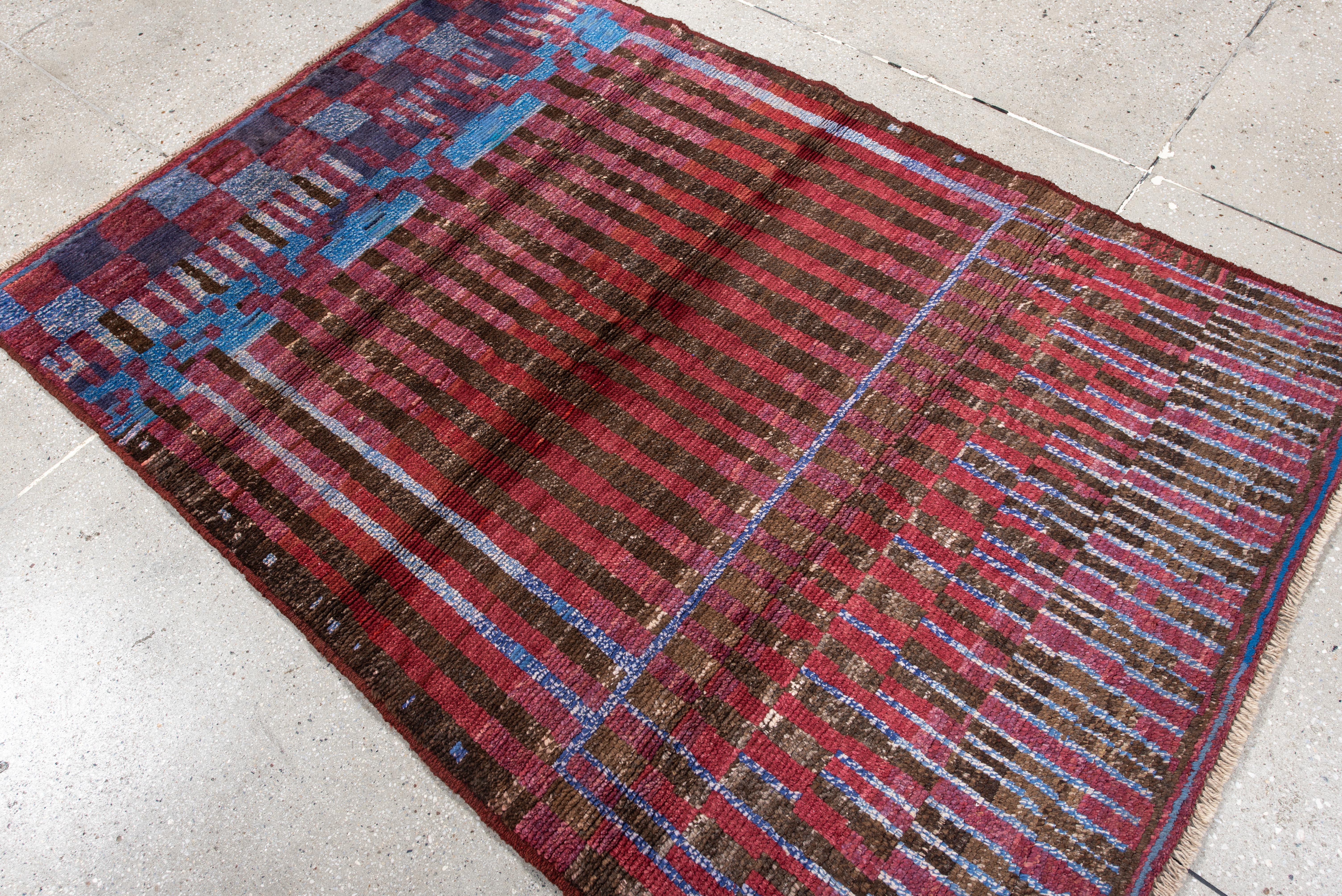 Esta llamativa alfombra marroquí presenta una espectacular interacción de motivos verticales y a cuadros, en una rica paleta de burdeos, marrón espresso y ciruela oscuro, salpicada de detalles en azul cobalto y lavanda pálido. El rayado rítmico