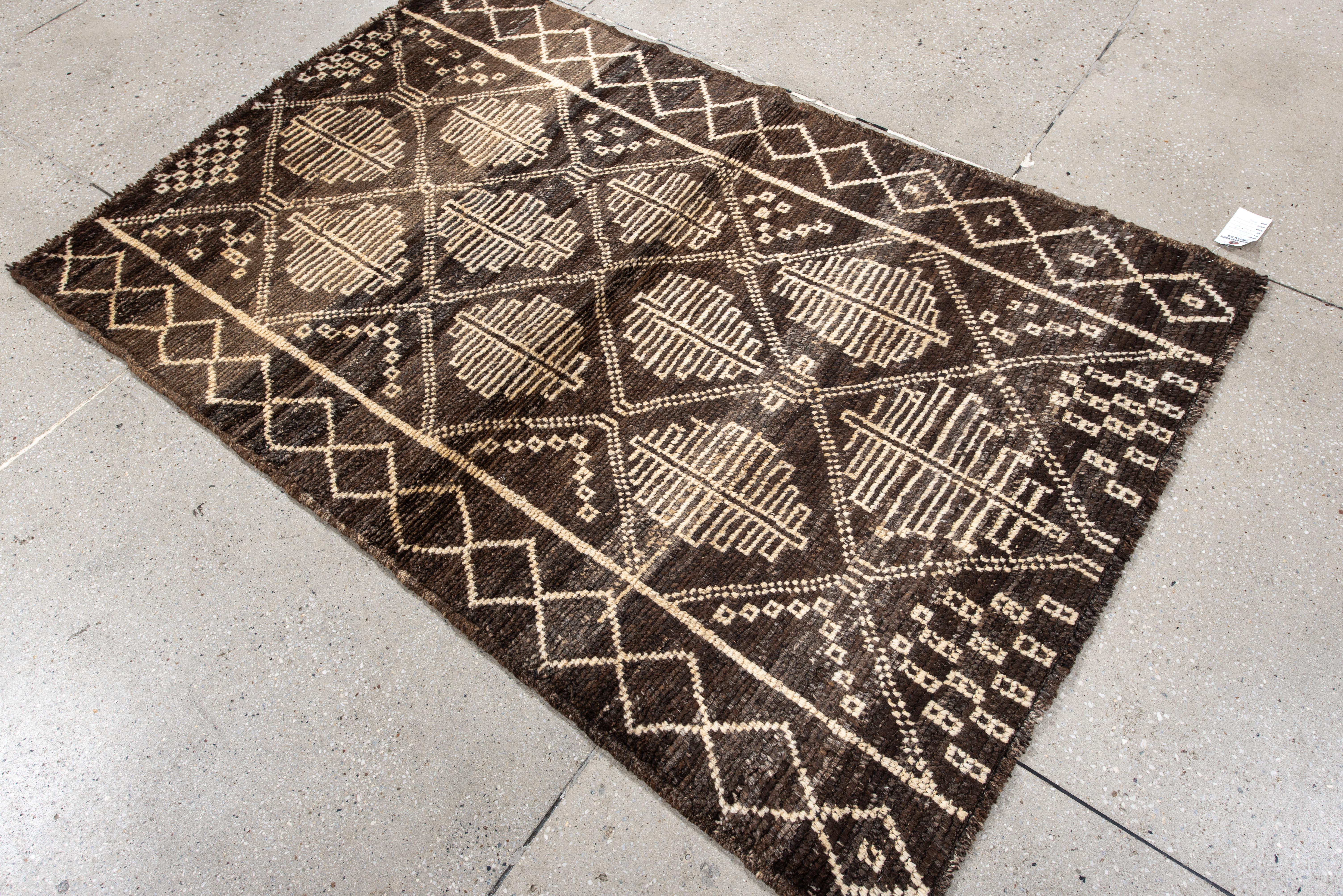 Esta alfombra marroquí de tonos intensos presenta un campo marrón espresso oscuro adornado con una rítmica cuadrícula de rombos tribales, cada uno de los cuales encierra estilizados motivos de hojas marfil. El suave contraste entre el fondo terroso