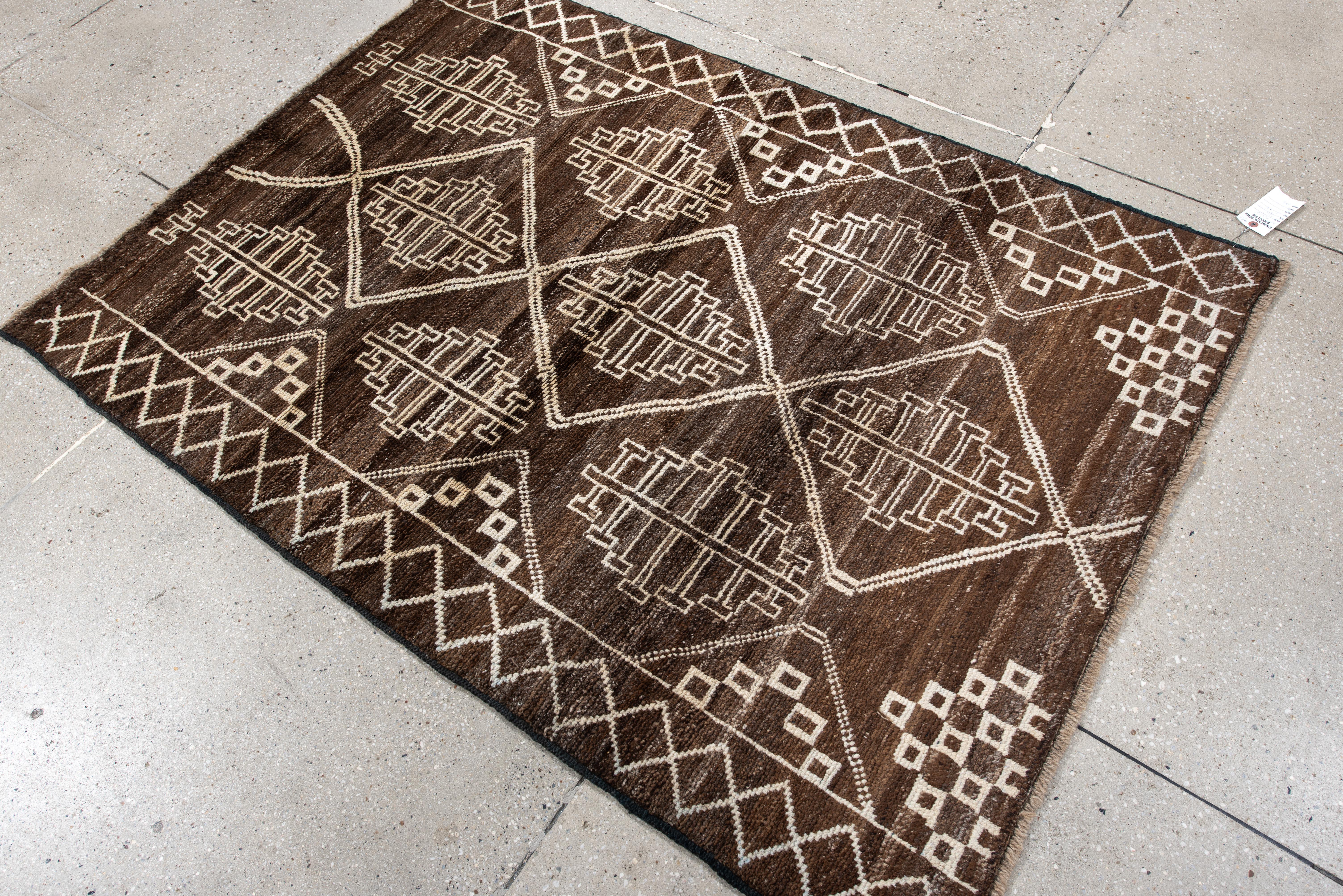 Esta llamativa alfombra marroquí presenta una atrevida cuadrícula geométrica en una refinada paleta de marrón espresso terroso y marfil nítido. Cada panel romboidal alberga un estilizado motivo de hoja bereber, flanqueado por acentos de damero y