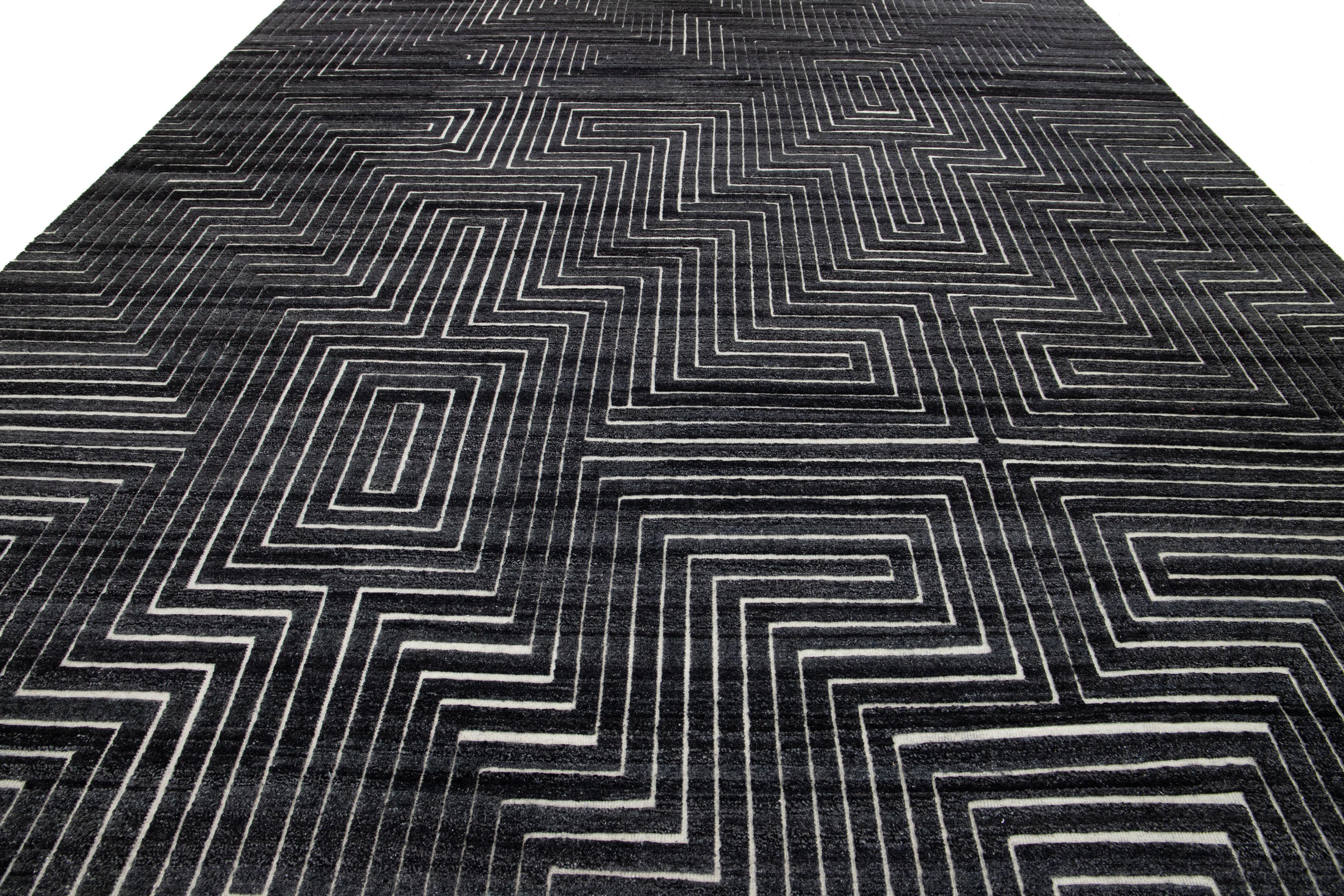 Dieser handgeknüpfte Wollteppich im modernen marokkanischen Stil zeichnet sich durch ein sattes anthrazitfarbenes Feld aus, das mit einem auffälligen weißen geometrischen Muster akzentuiert ist. Dieses schöne Stück wird die Ästhetik eines jeden