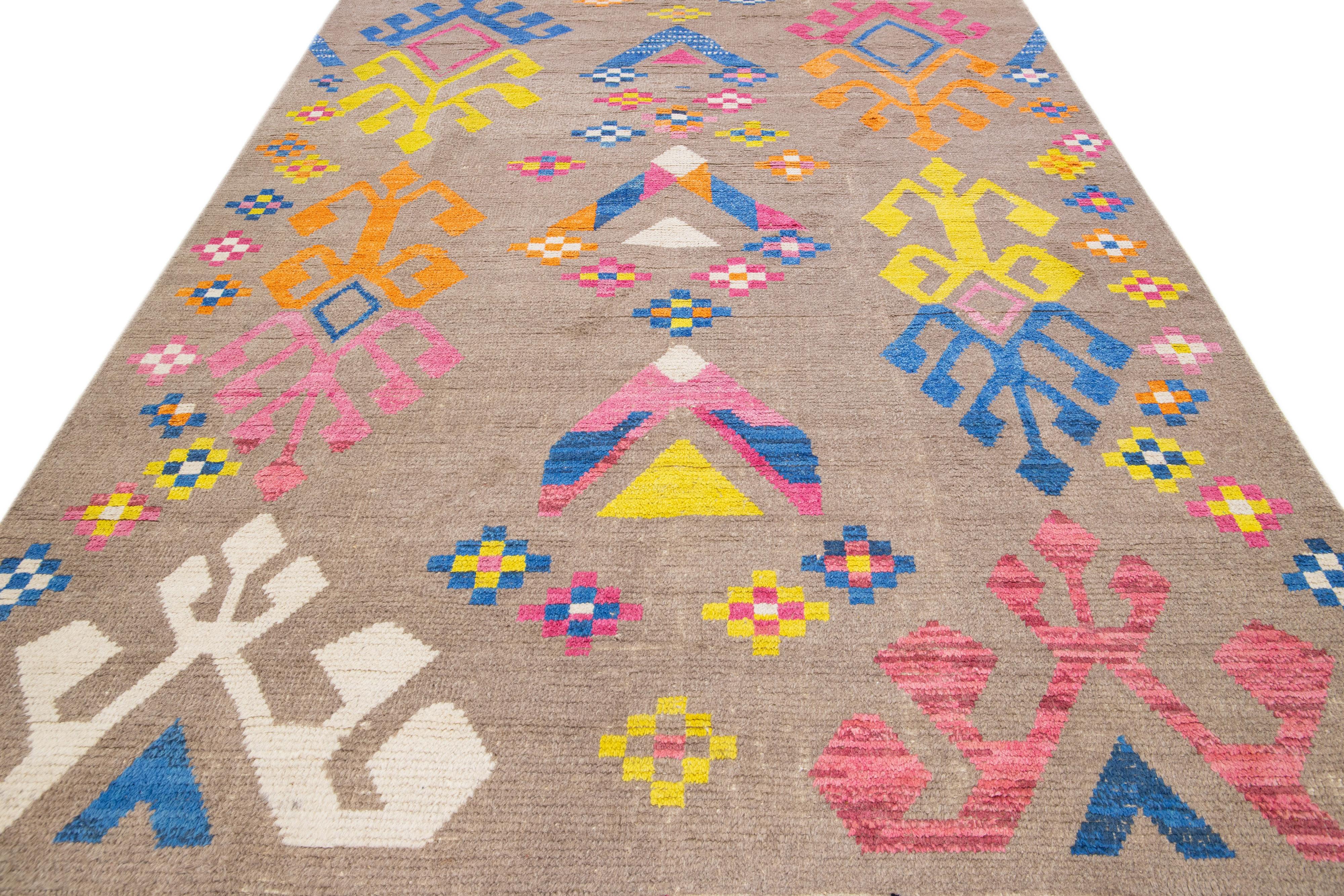 Beautiful modern Moroccan-style hand-knotted wool rug with a beige field and fringes on the top and bottom end. This piece has orange, blue, gray, and yellow accent colors in a gorgeous tribal design.

This rug measures 8' x 10'5