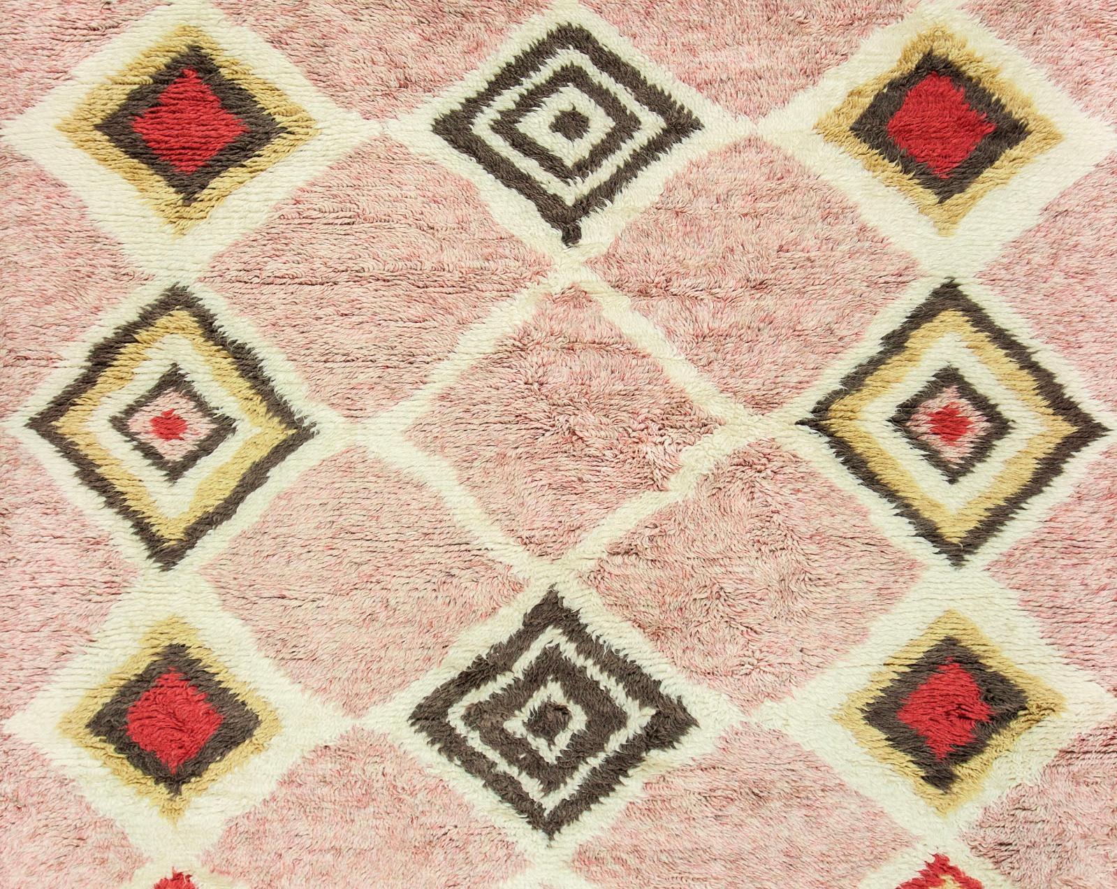 This contemporary Moroccan style pink and ivory rug features a geometric diamond pattern in triangles of gold, brown and red and is fringed on two ends. This highly durable rug with a plush heathery, colored pile is hand knotted from the finest wool