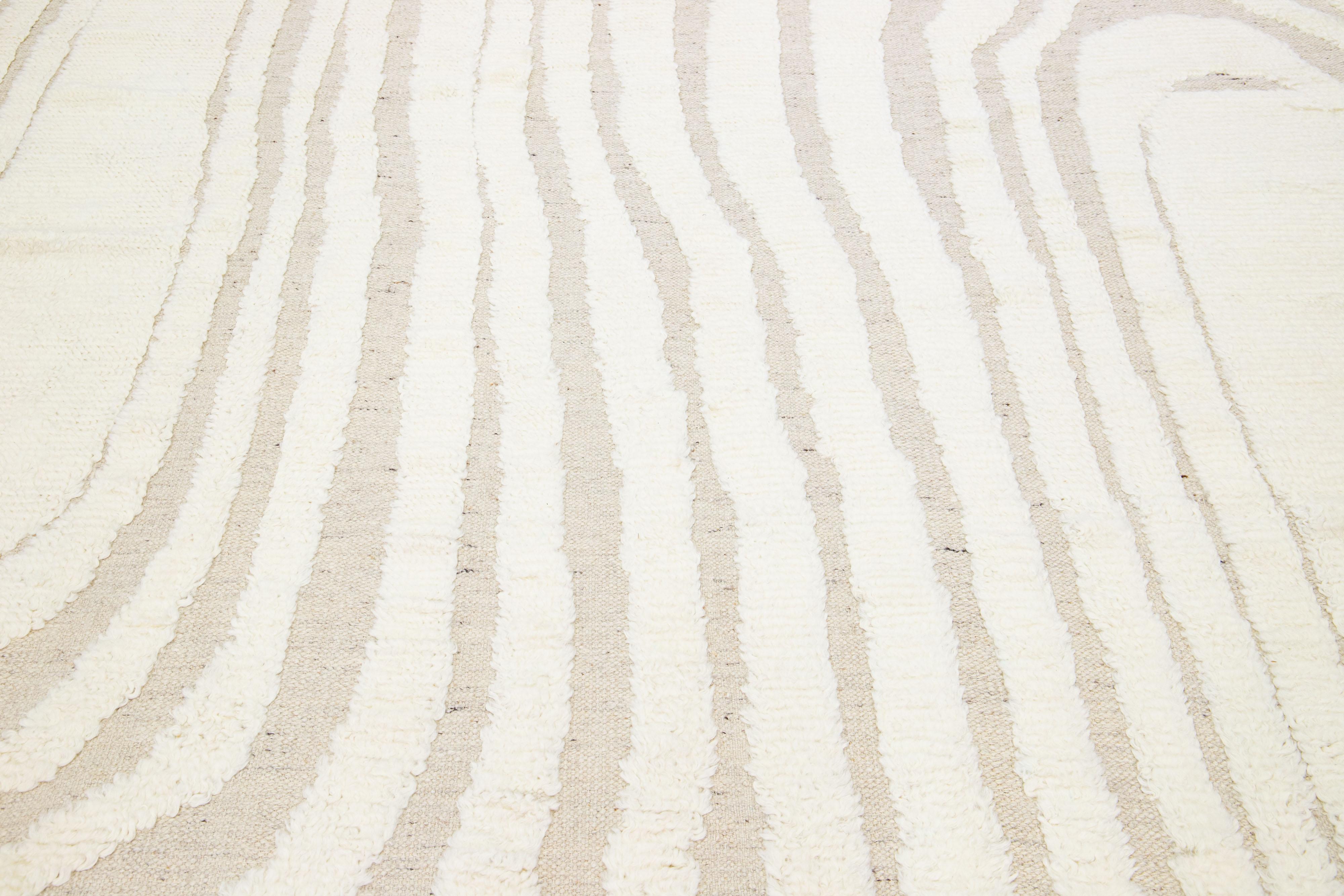This hand-knotted wool rug exhibits a sophisticated contemporary Moroccan motif, gracefully displayed in a serene and understated Ivory hue. Masterfully arranged against a captivating background of beige, the harmonious interplay of these