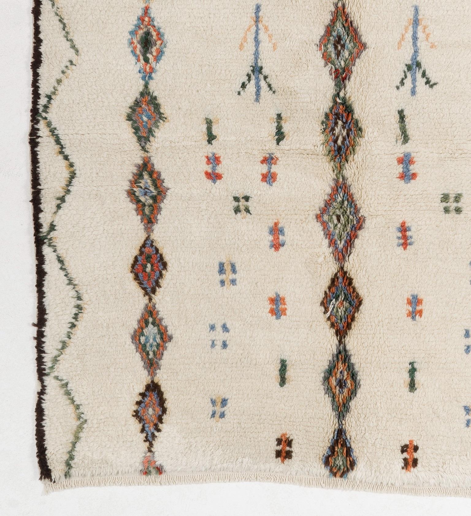A contemporary hand knotted Moroccan rug made of natural un-dyed sheep's wool with three columns of delicately drawn linked-diamonds and free-floating comb and fishbone motifs in between the columns in dark green, light blue, salmon pink, salmon