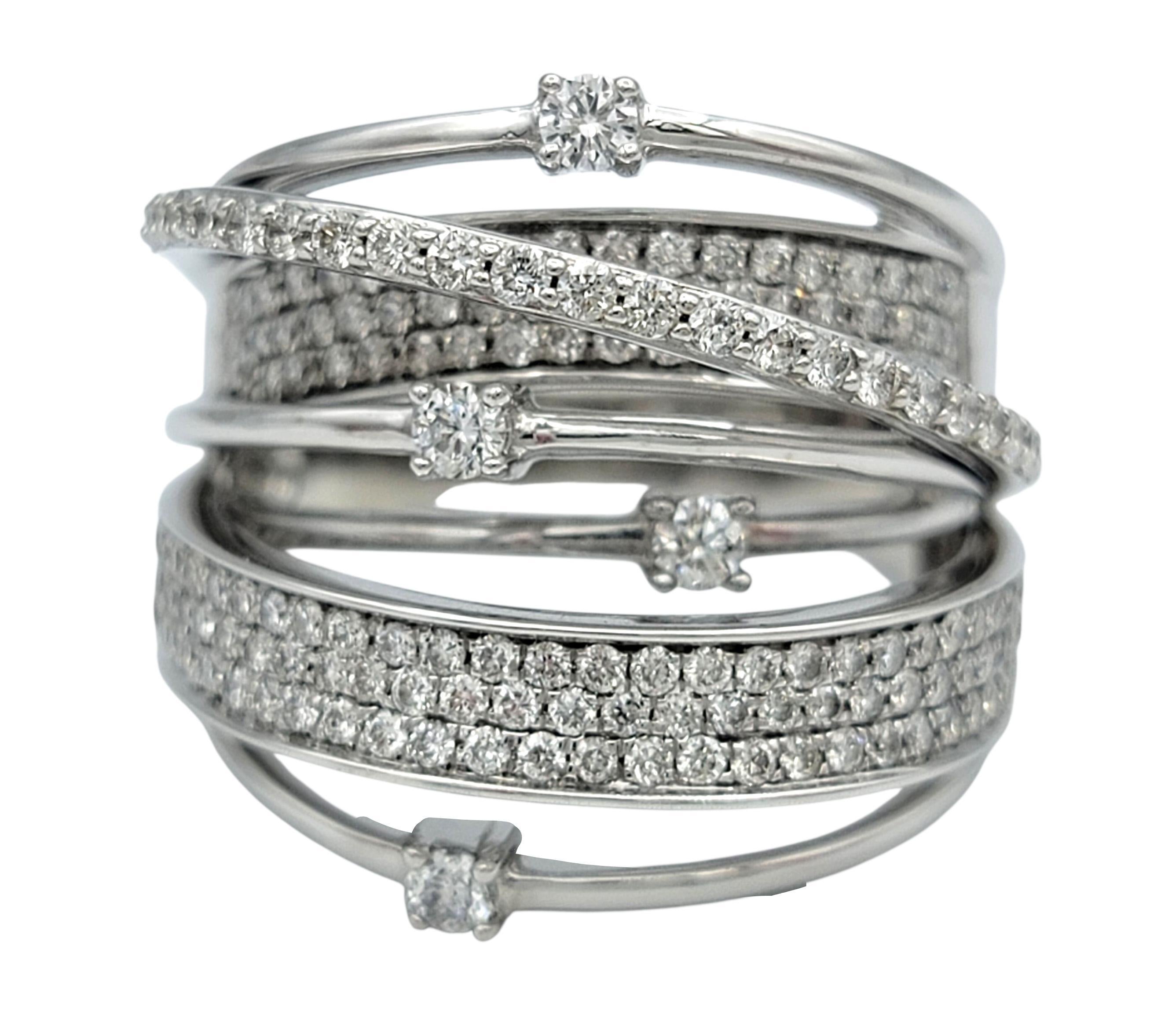 This diamond ring features a layered, wrap-style design that creates a striking sense of movement around the finger. Multiple rows of shimmering diamonds sweep across the band, giving the piece a luxurious, textured appearance. The alternating