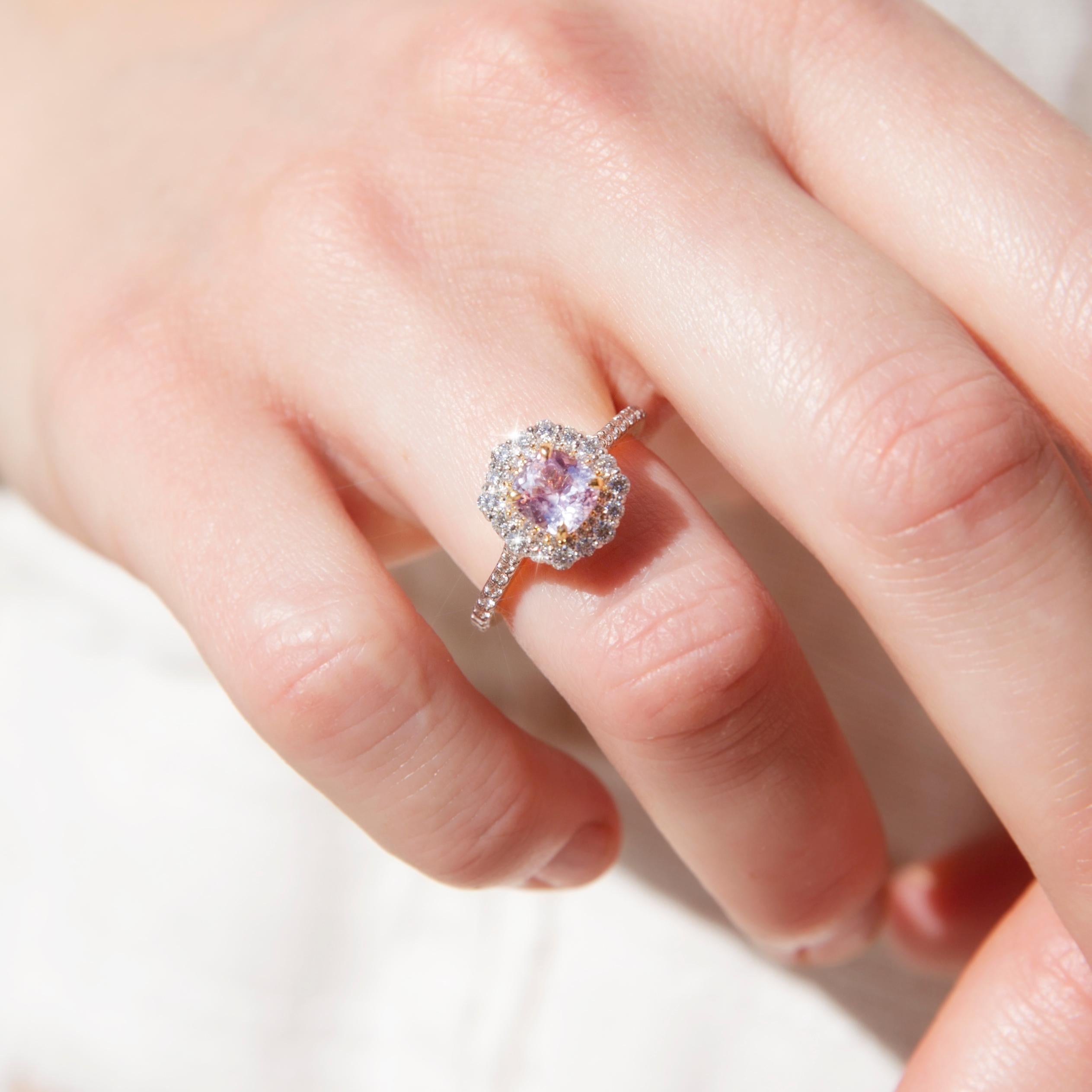 Forged in gleaming 18 carat gold, this stunning contemporary ring sees an enchanting halo cluster with a light pink sapphire set carefully within a shimmering border of round brilliant cut diamonds and with diamonds running down the elegant