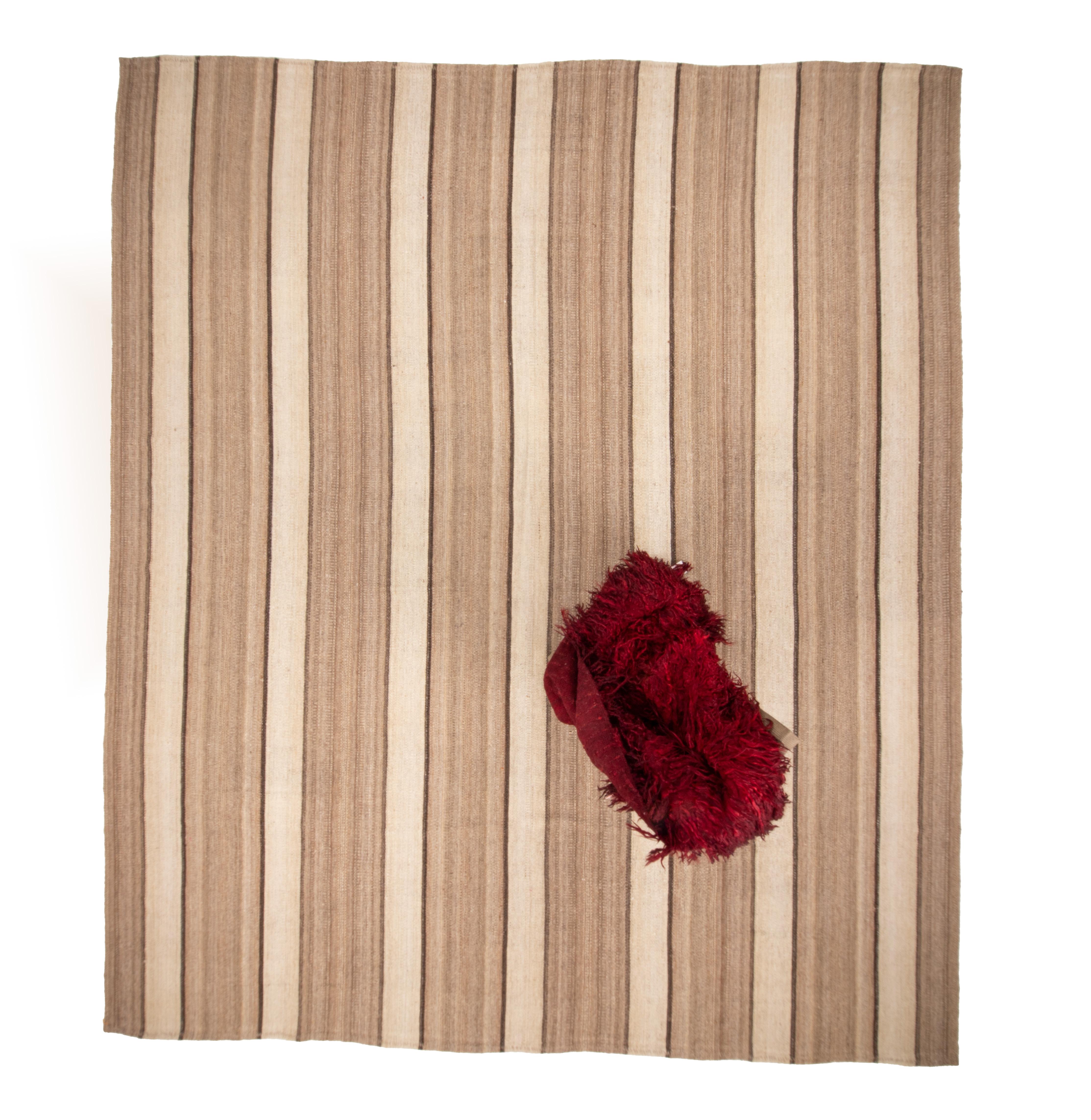 Ce kilim est tissé avec des fils de laine non teints en bandes étroites, puis cousu à la main. Il est doté d'une poignée souple.

