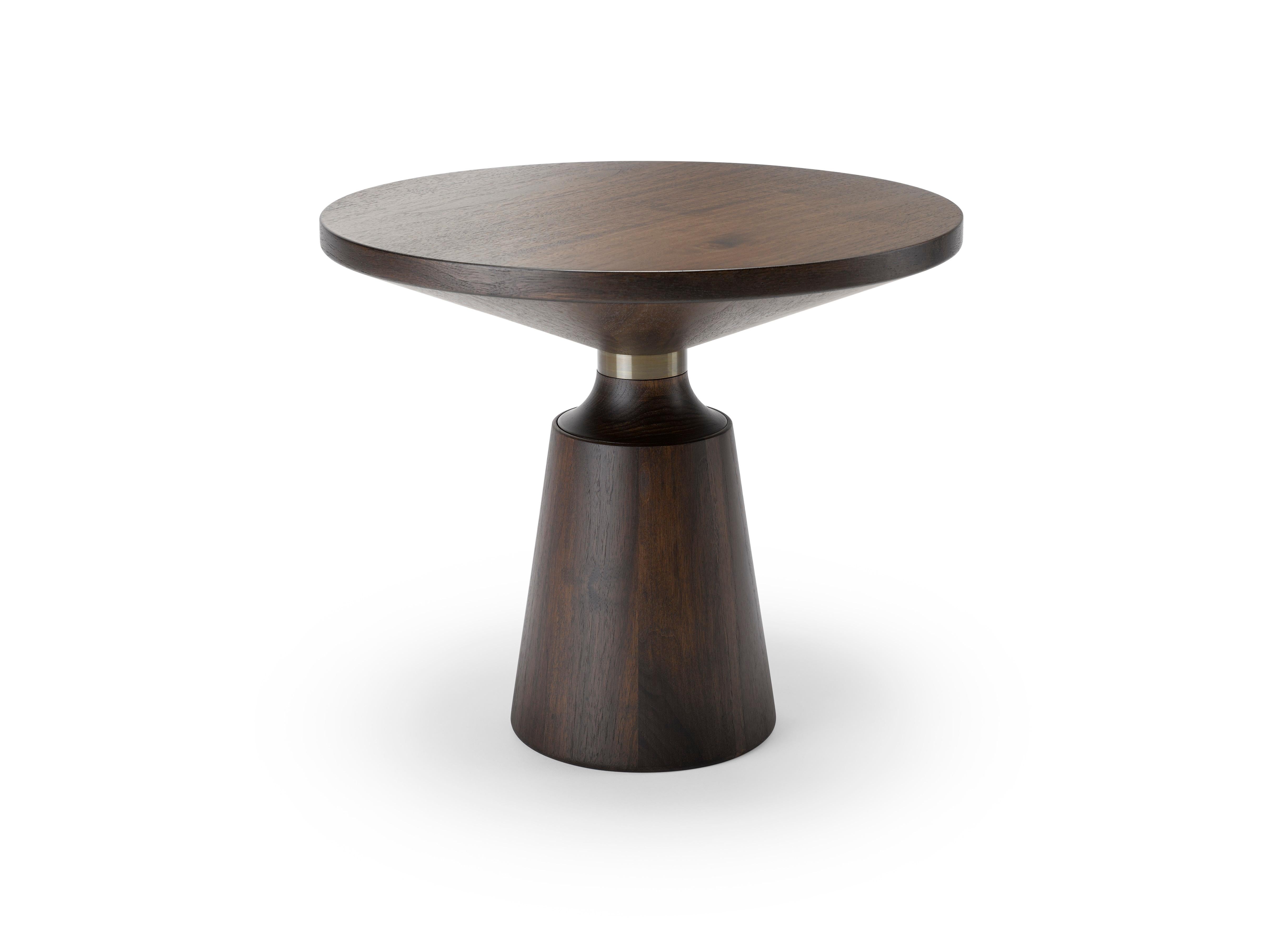 Tornito a mano e utilizzando sia legno massiccio che impiallacciato, il Tavolo Occasionale Nicole ha una silhouette semplice ma di grande impatto grafico, punteggiata dal collare in metallo. Il tavolino da salotto Nicole è mostrato qui in noce