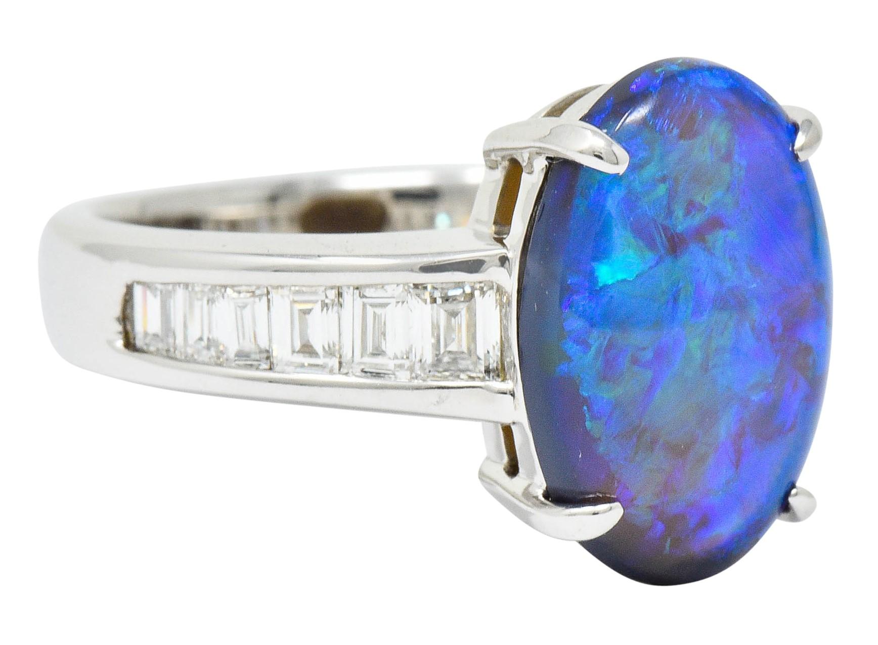 Centering an oval cut opal cabochon measuring approximately 13.5 x 9.2 mm

Basket set and translucent with strong violet, blue, green play-of-color

Shoulders are channel set with baguette cut diamonds

Weighing in total approximately 1.27 carats
