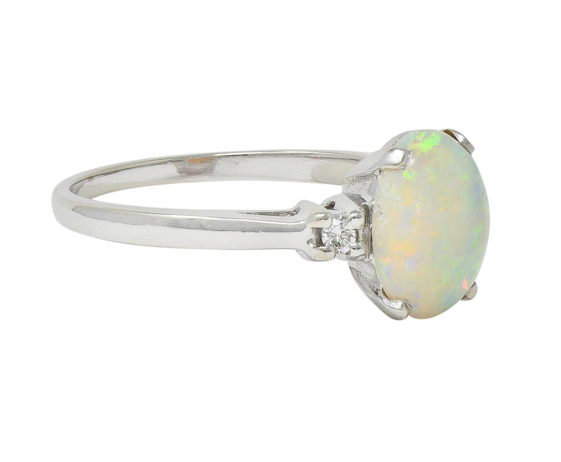 Zentrierung eines ovalen Opal-Cabochons von 8,0 x 10,0 mm
Transluzente weiße Körperfarbe mit spektralem Farbenspiel 
In einem Korb gefasst und von Kathedralschultern flankiert
Zackenbesetzt mit runden Diamanten im Brillantschliff 
Mit einem
