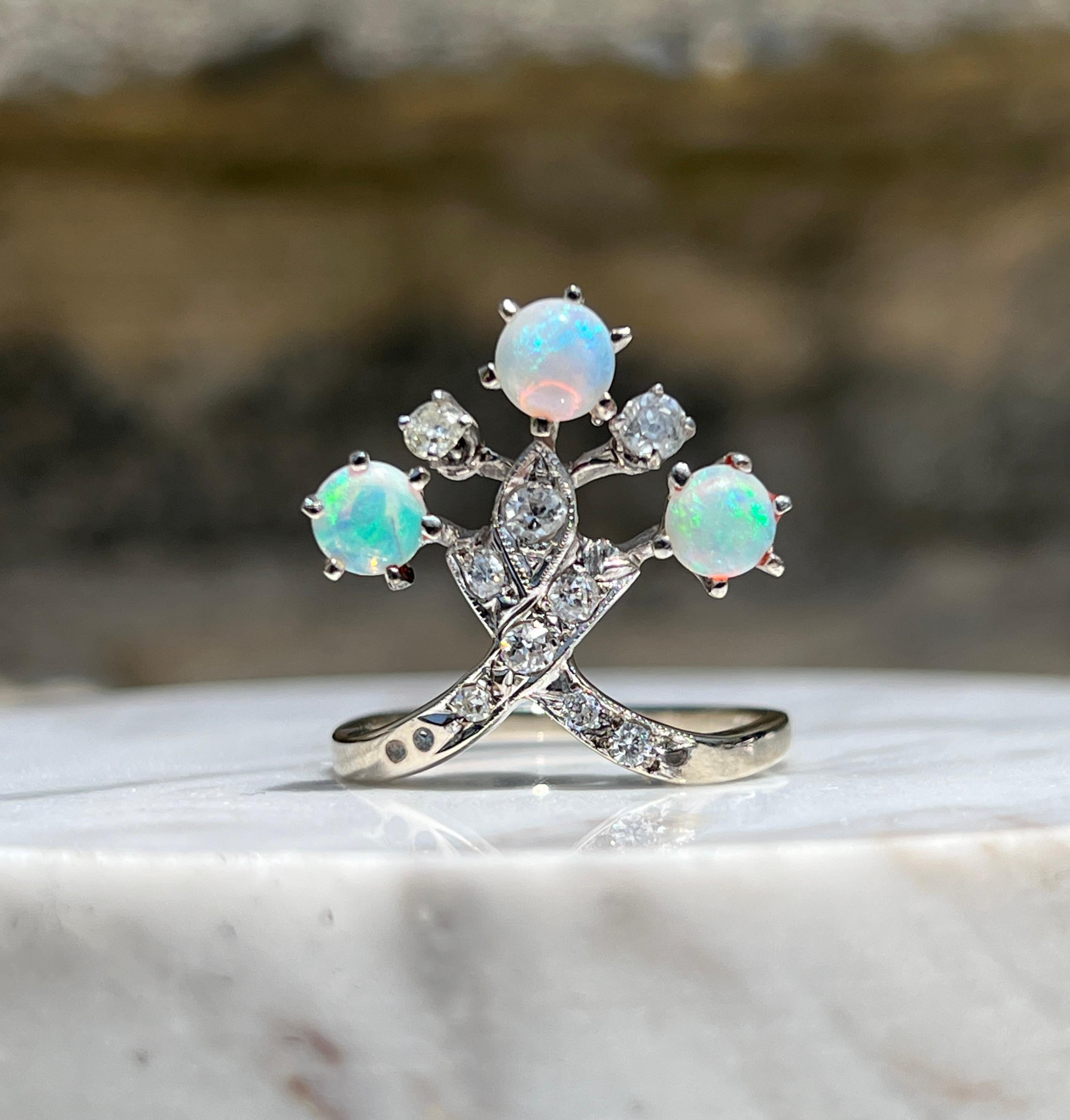 Ein zeitgenössischer Ring aus glänzendem 14-karätigem Weißgold mit einem skurrilen, himmlisch inspirierten Design. Dieses bezaubernde Stück zeigt drei leuchtende runde Opale von je 4,5 mm Größe, die bei jeder Bewegung ein faszinierendes blaues,